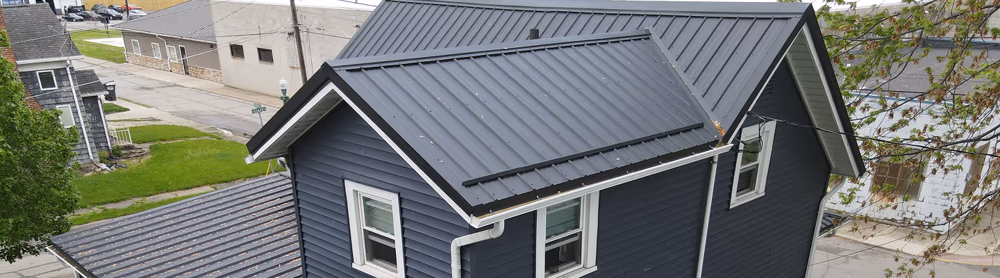Dark blue house with a metal roof in a residential neighborhood.