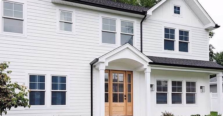 Front view of a modern white two-story house with multiple windows and a wooden front door under a small gabled porch.
