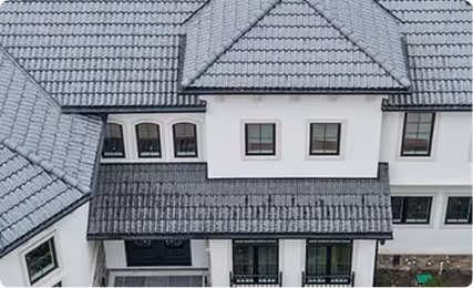 Aerial view of a large white house with multiple gray tiled roofs of varying shapes and angles.