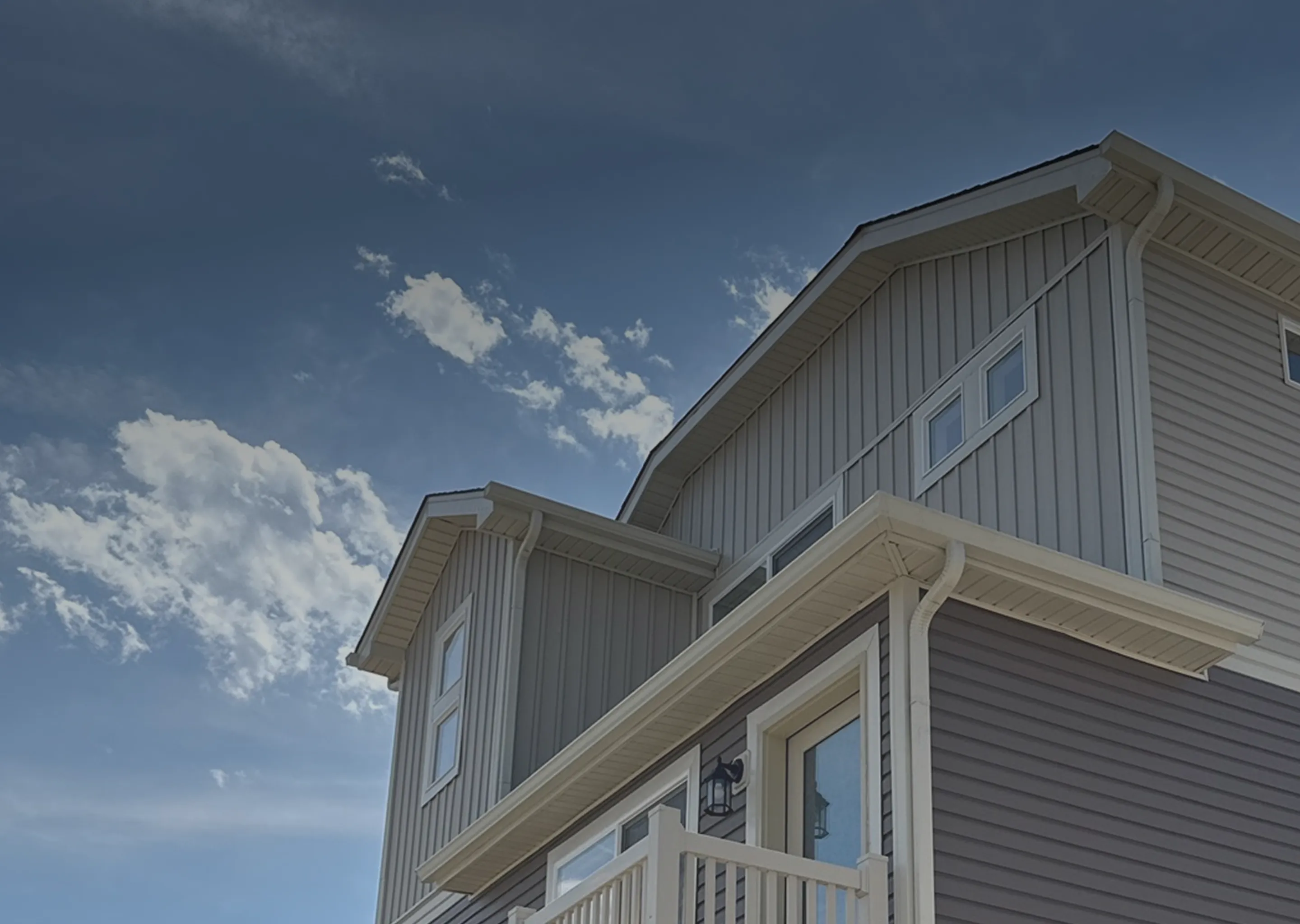 Gray two-story house with white trim and a balcony against a partly cloudy blue sky.
