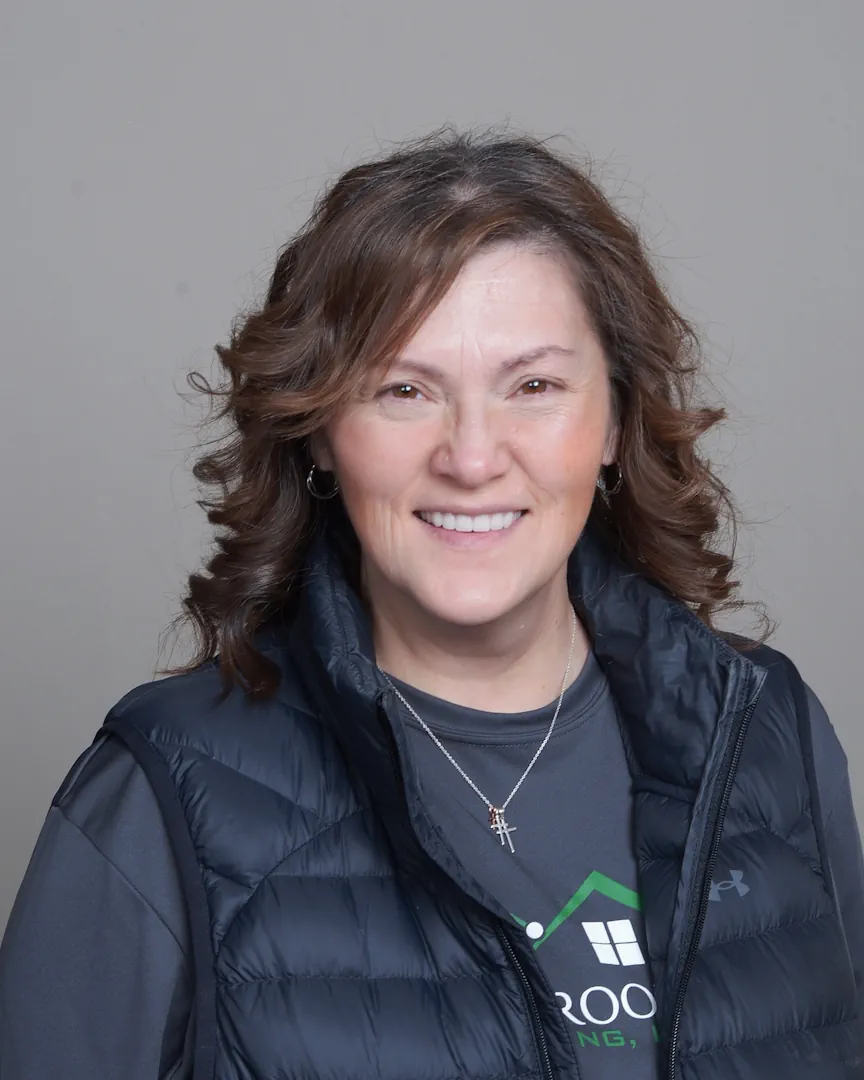 Smiling woman with curly brown hair wearing a black puffer vest and a gray shirt with a necklace.