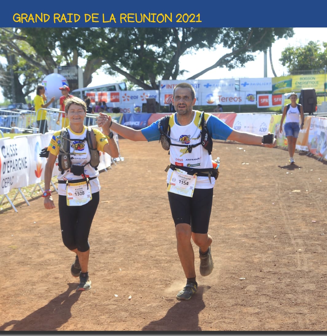Deux coureurs main dans la main franchissent la ligne d'arrivée du Grand Raid de la Réunion 2021 sur un chemin de terre.