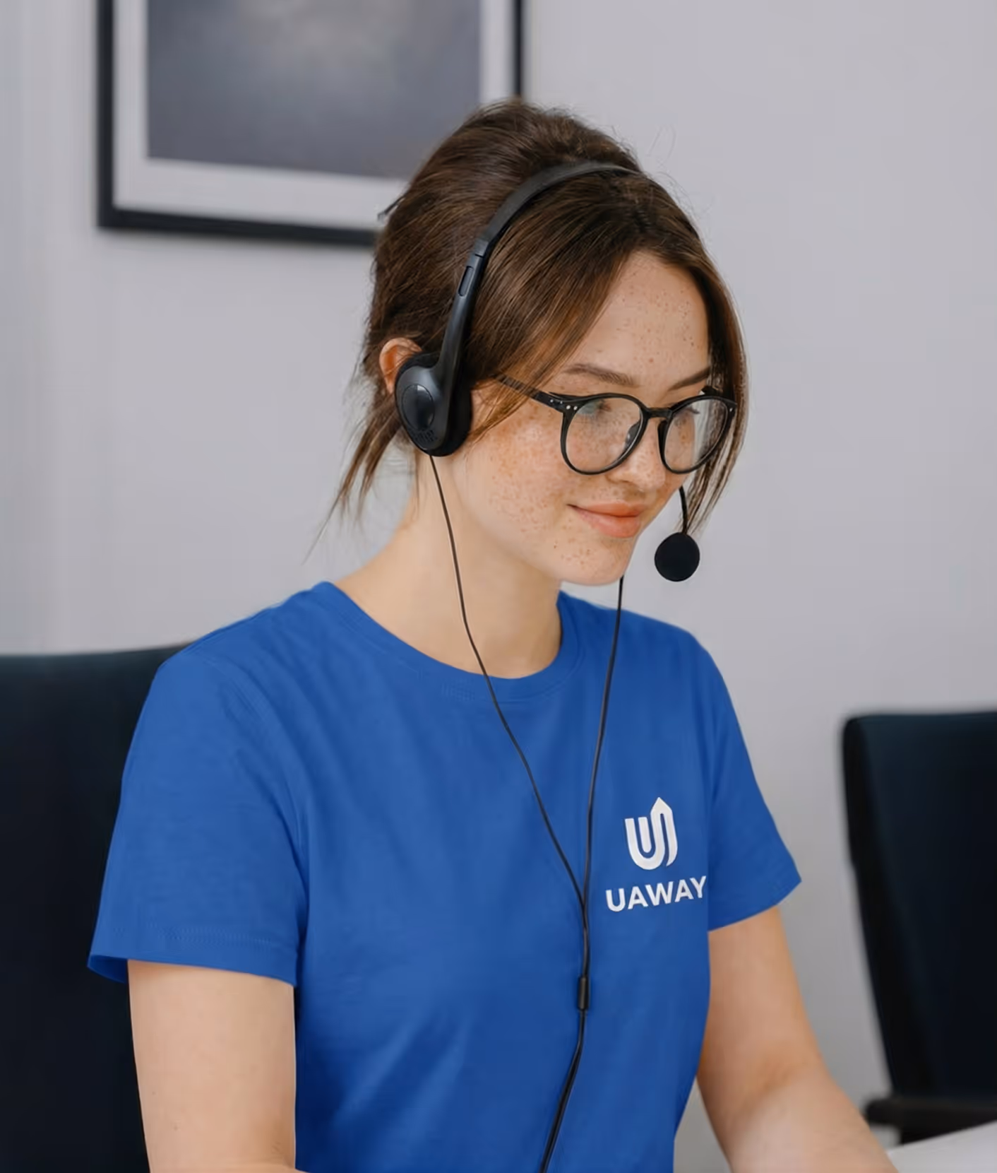 Young woman with glasses wearing a headset and blue UAWAY t-shirt working.
