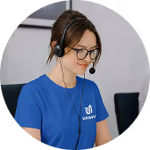 Woman wearing glasses and a blue headset, working at a computer, dressed in a blue t-shirt with a white logo.