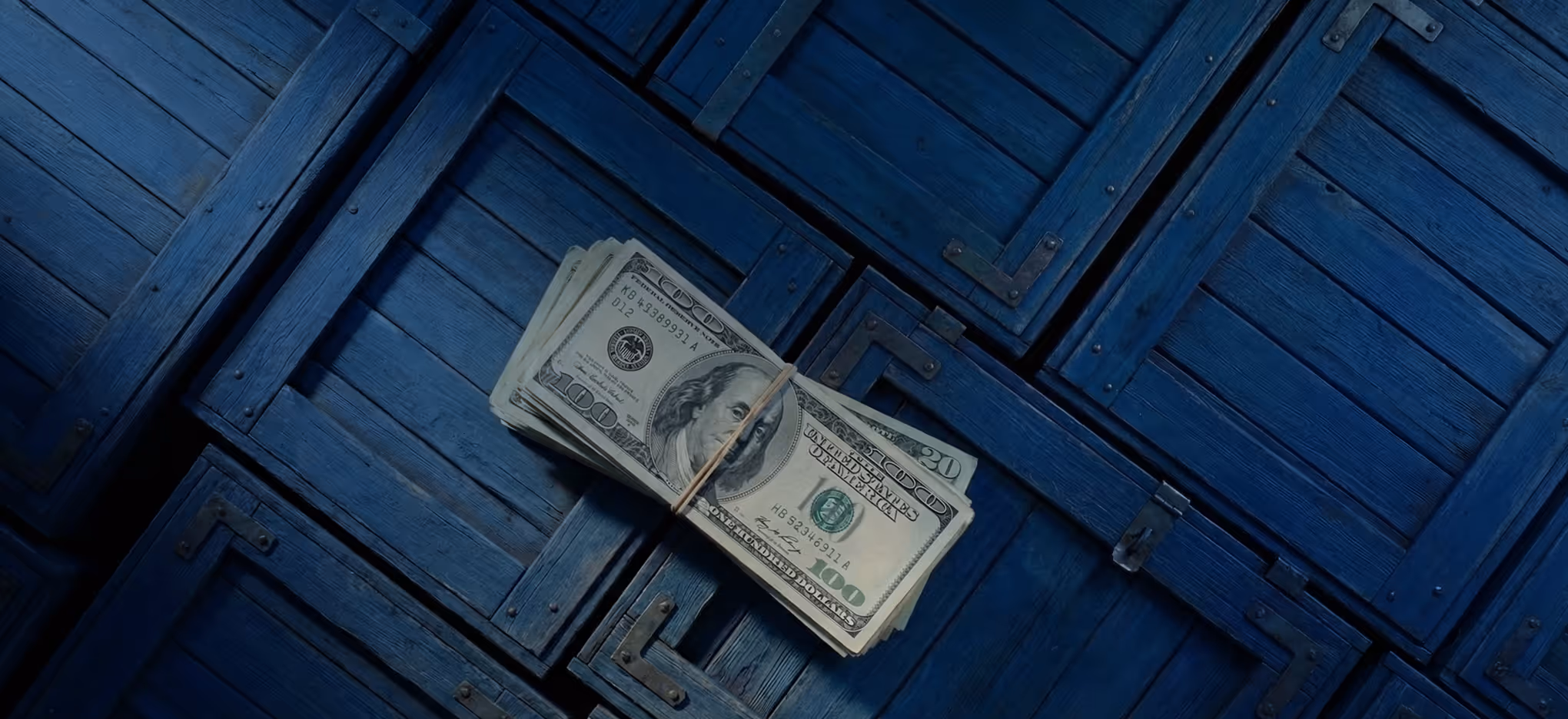 Stack of US dollar bills held together by a rubber band on a blue wooden surface.