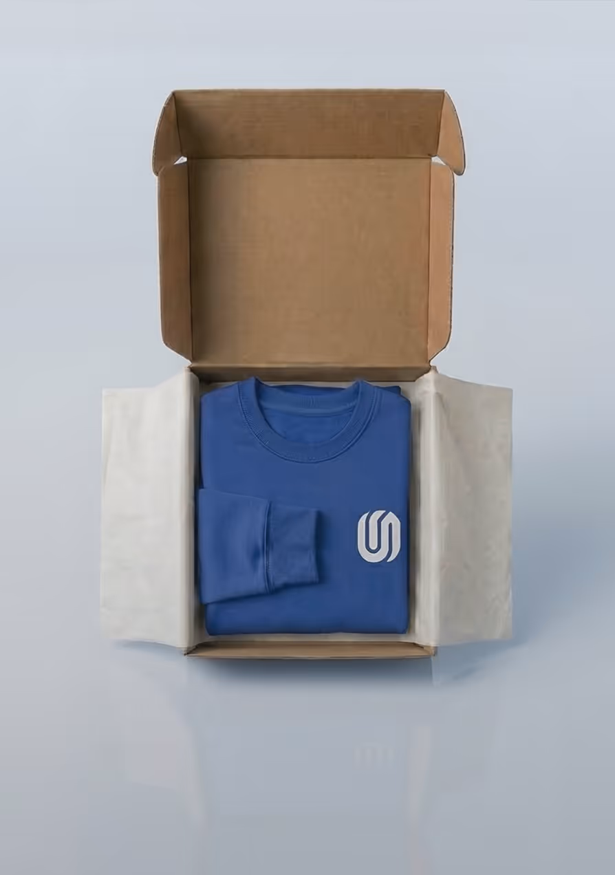 Blue sweatshirt with white logo folded inside an open cardboard box with white tissue paper.