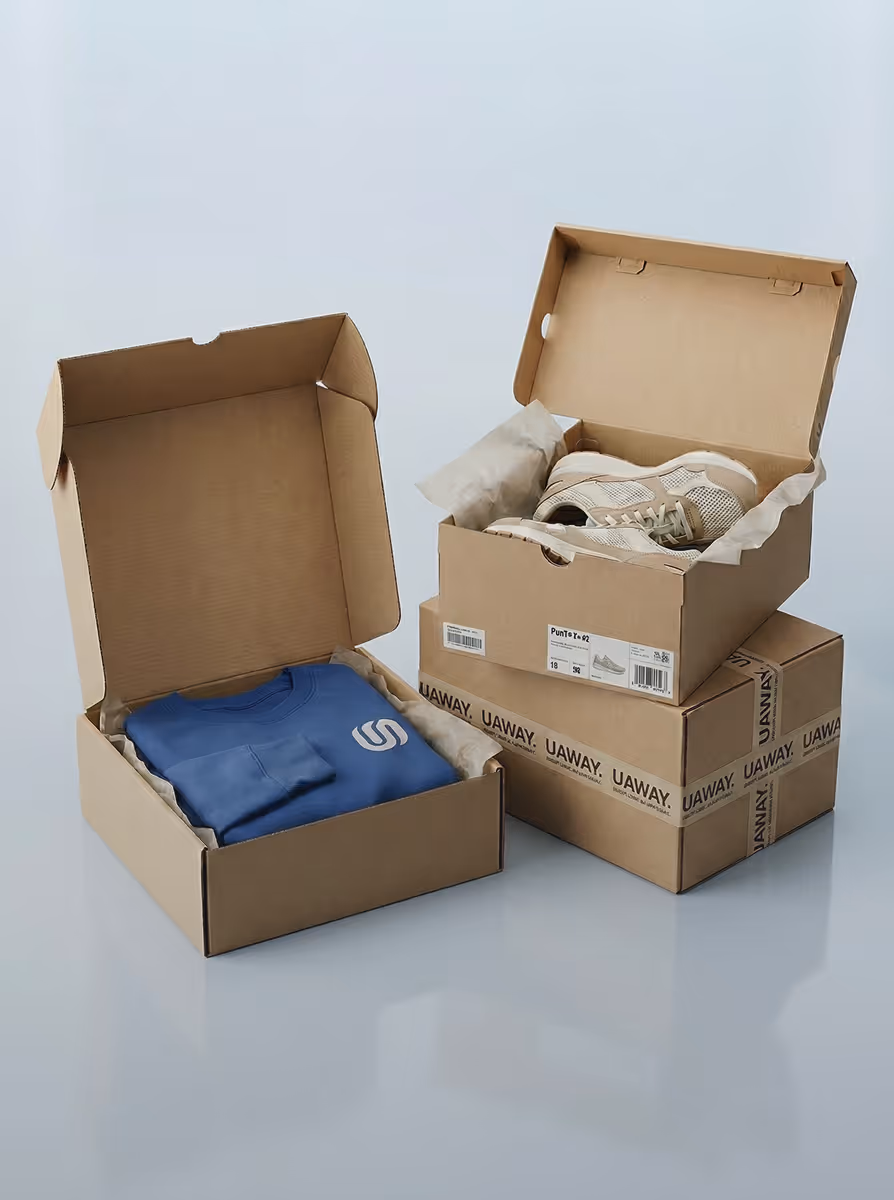 Open cardboard boxes with one containing a folded blue sweatshirt and another holding a pair of beige sneakers, stacked on two closed boxes with UAWAY branding.