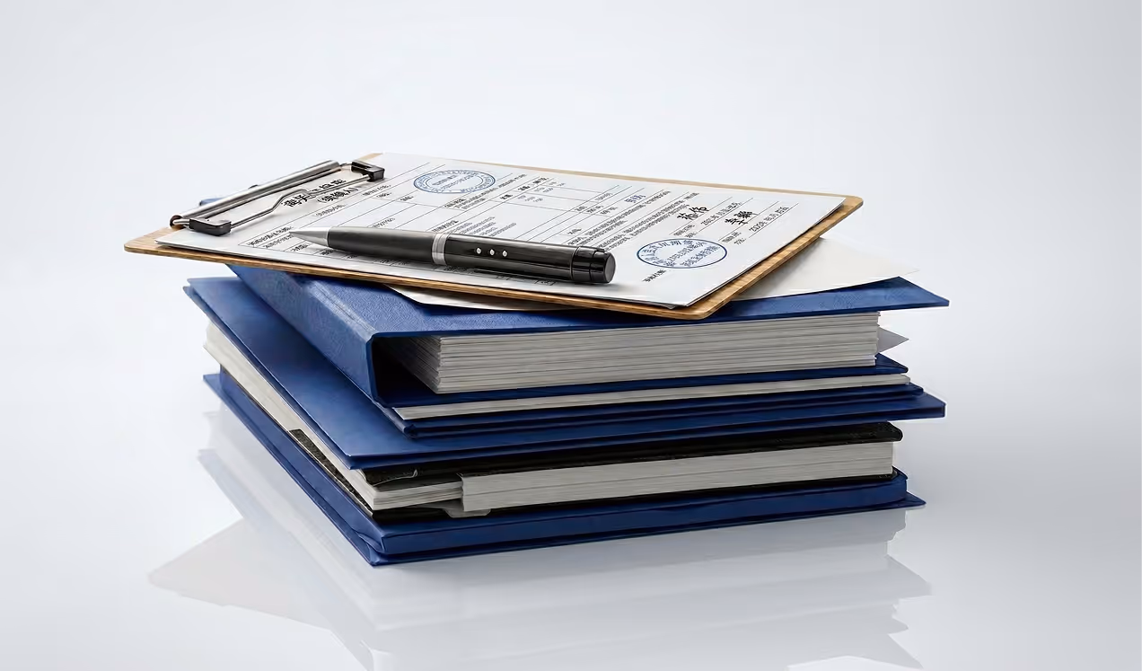 Stack of blue binders with a clipboard holding a document and a black pen on top.