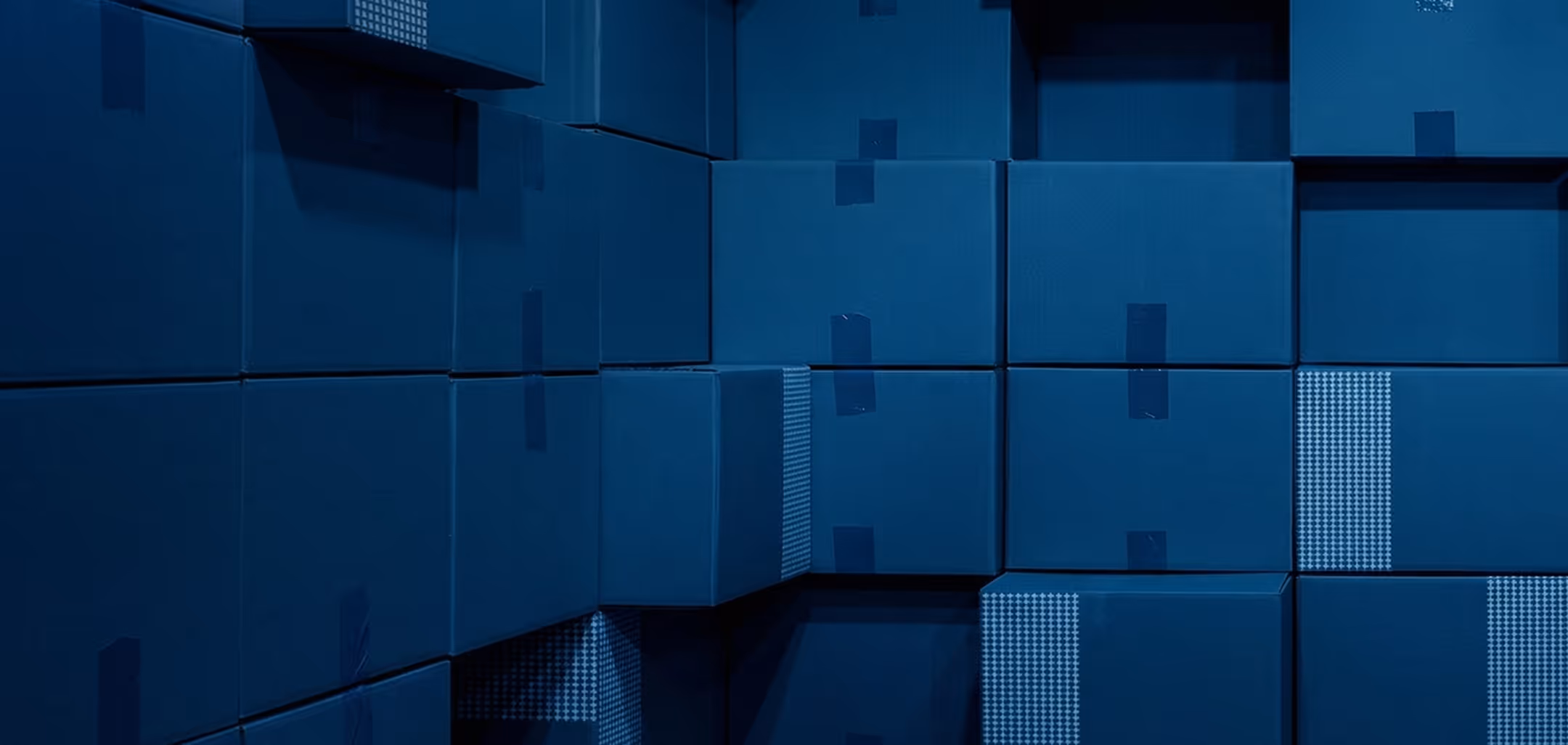 Stacked blue cardboard boxes with some featuring patterned tape on a dark surface.