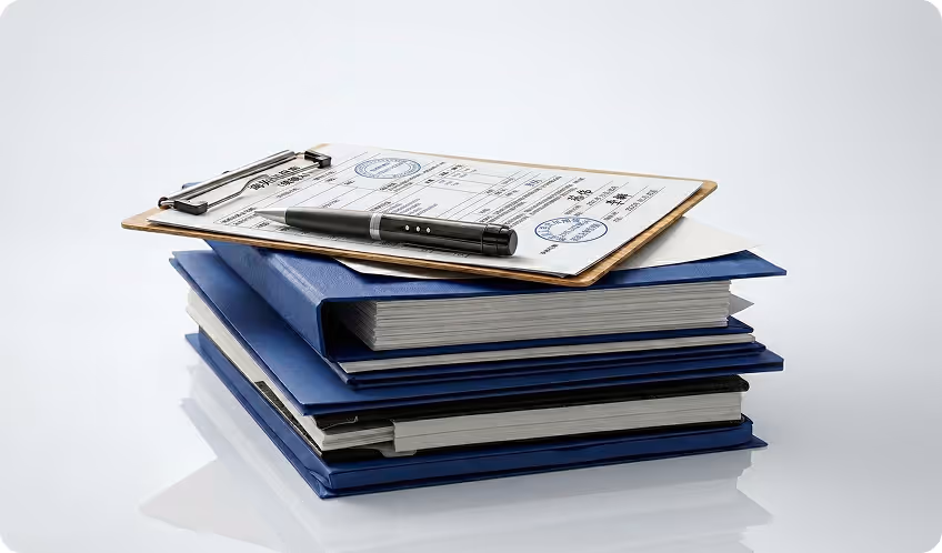 Stack of blue binders with a clipboard holding documents and a black pen on top.
