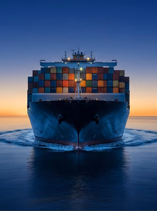 Front view of a large container ship on calm water during sunset with colorful cargo containers stacked on deck.