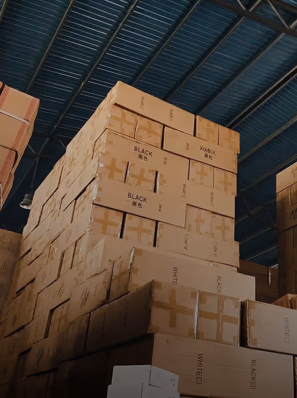 Tall stack of cardboard boxes labeled with 'BLACK' and 'WHITE' inside a warehouse with a metal roof.