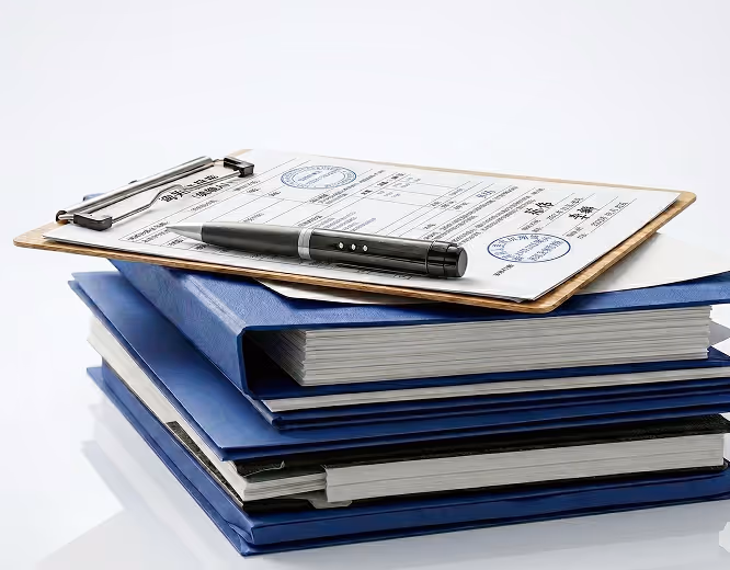 Stack of blue binders with a clipboard on top holding a document and a black pen resting on it.