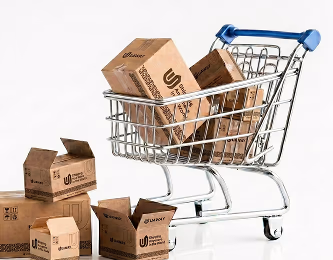Miniature shopping cart filled with cardboard shipping boxes and additional boxes scattered beside it on a white background.
