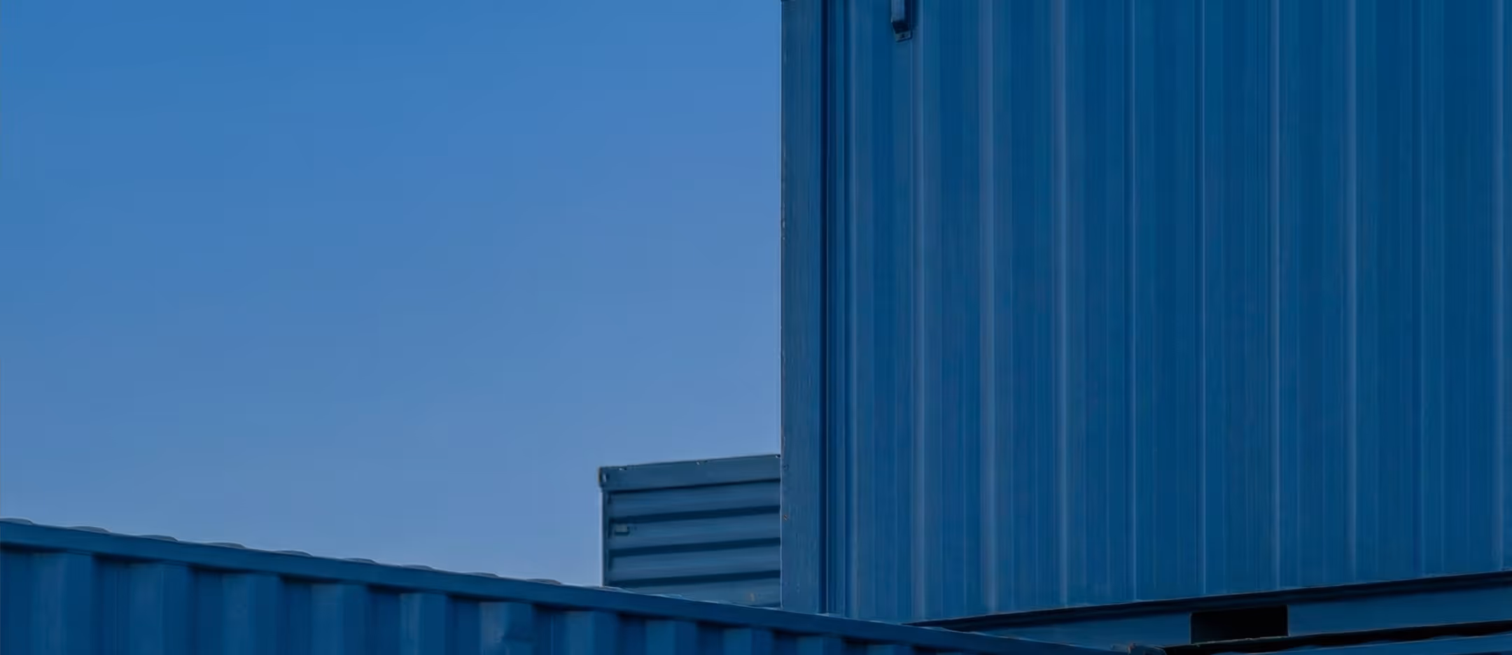 Close-up of blue industrial metal shipping containers under a clear blue sky.