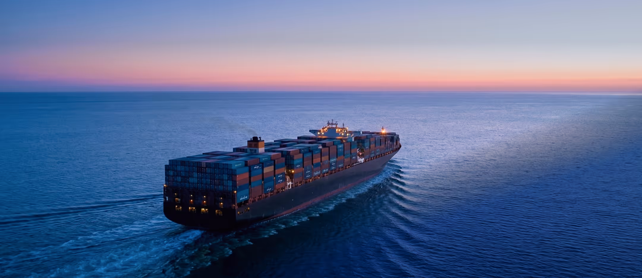 Large cargo container ship sailing on calm ocean waters during sunset.
