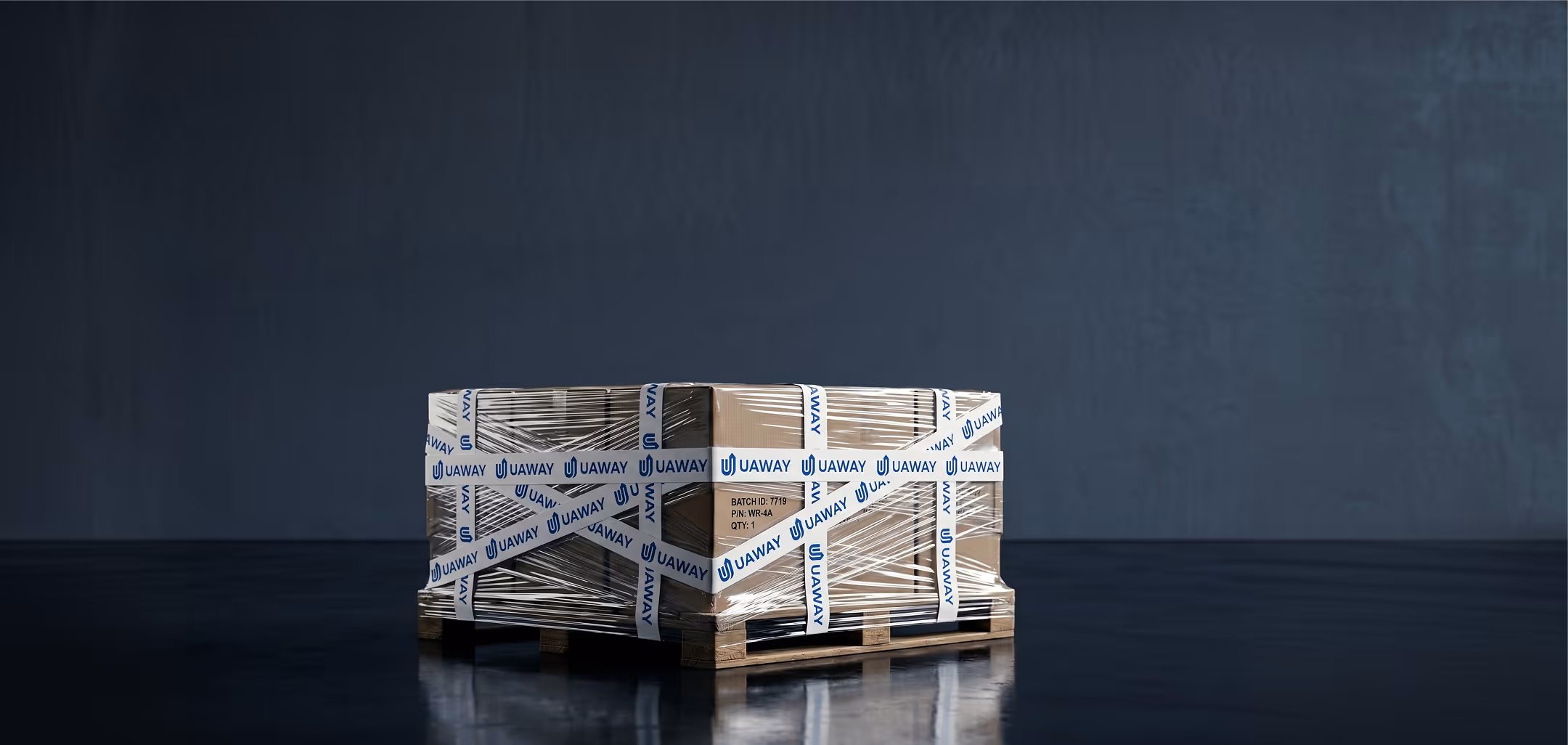 Wooden pallet with cardboard boxes wrapped in clear plastic and white tape labeled UAWAY on a reflective dark floor against a dark gray background.