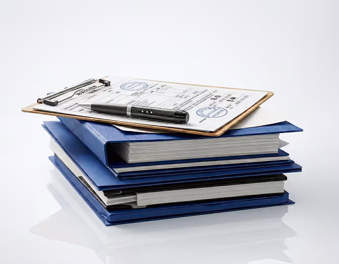 Stack of blue folders with documents on top clipped to a clipboard alongside a black pen.