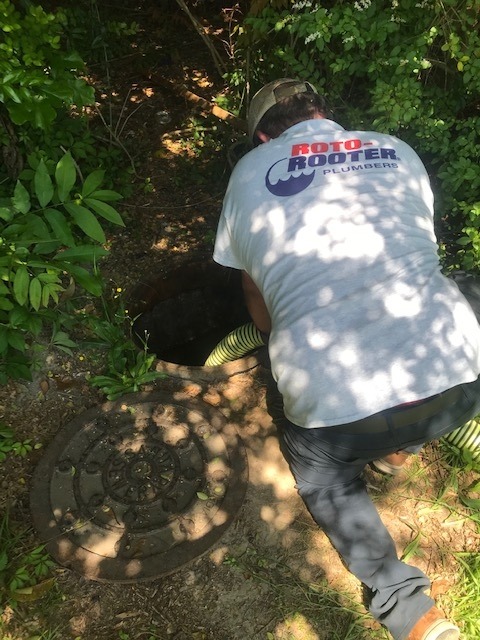 Plumber inserting a hose into a manhole for sewer line inspection or repair in Charleston, SC