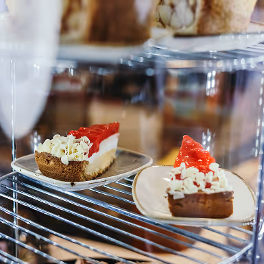 Twee stukken aardbeientaart met slagroom op witte bordjes in een glazen displaykast.