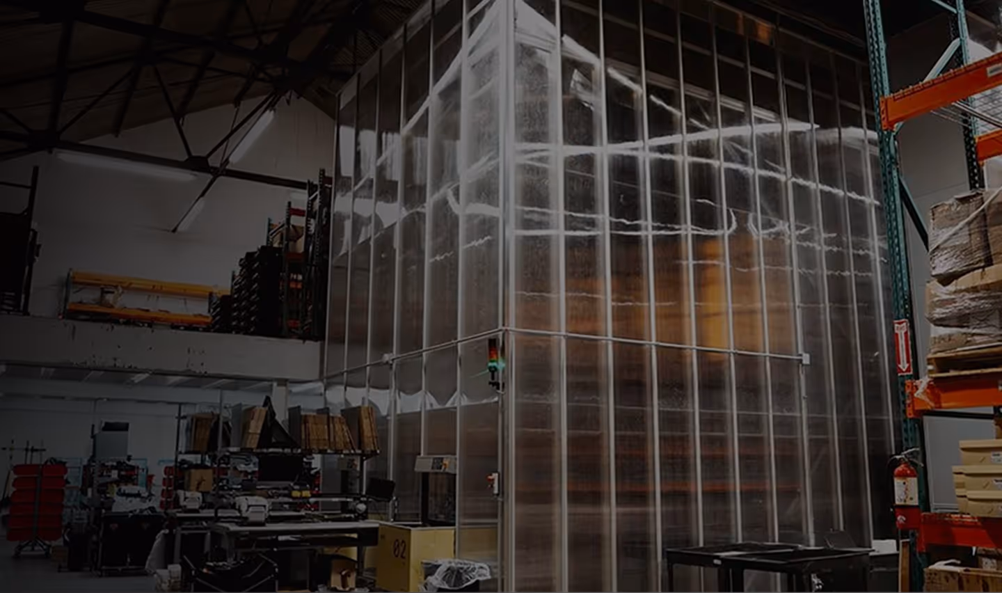 Interior of a warehouse with large transparent plastic curtains enclosing a section and industrial shelving around.