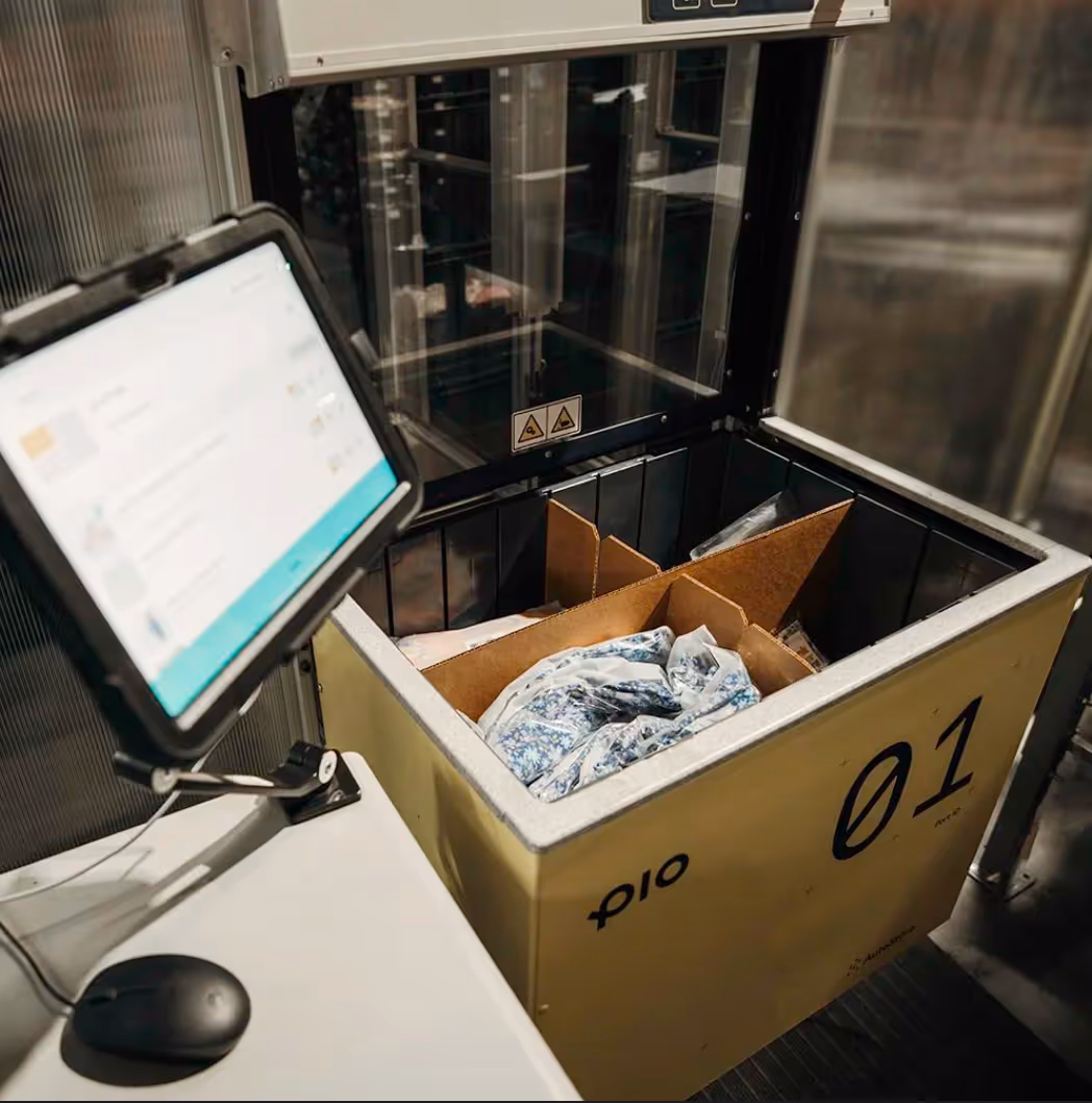 Open yellow storage bin labeled '01' containing a cardboard box with folded clothing inside, next to a computer monitor and mouse in an industrial setting.