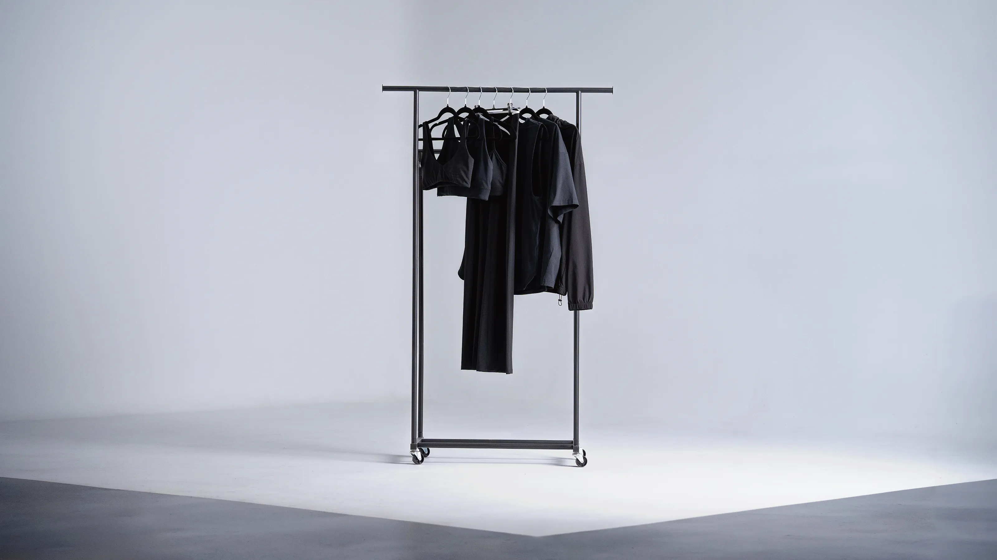 Black athletic wear items hanging on a rolling metal clothing rack against a plain backdrop.