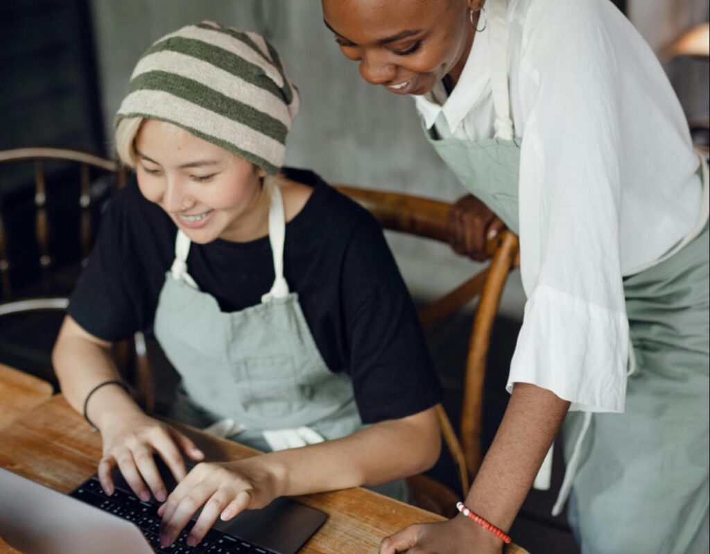 Two cafe workers smiling together at a laptop