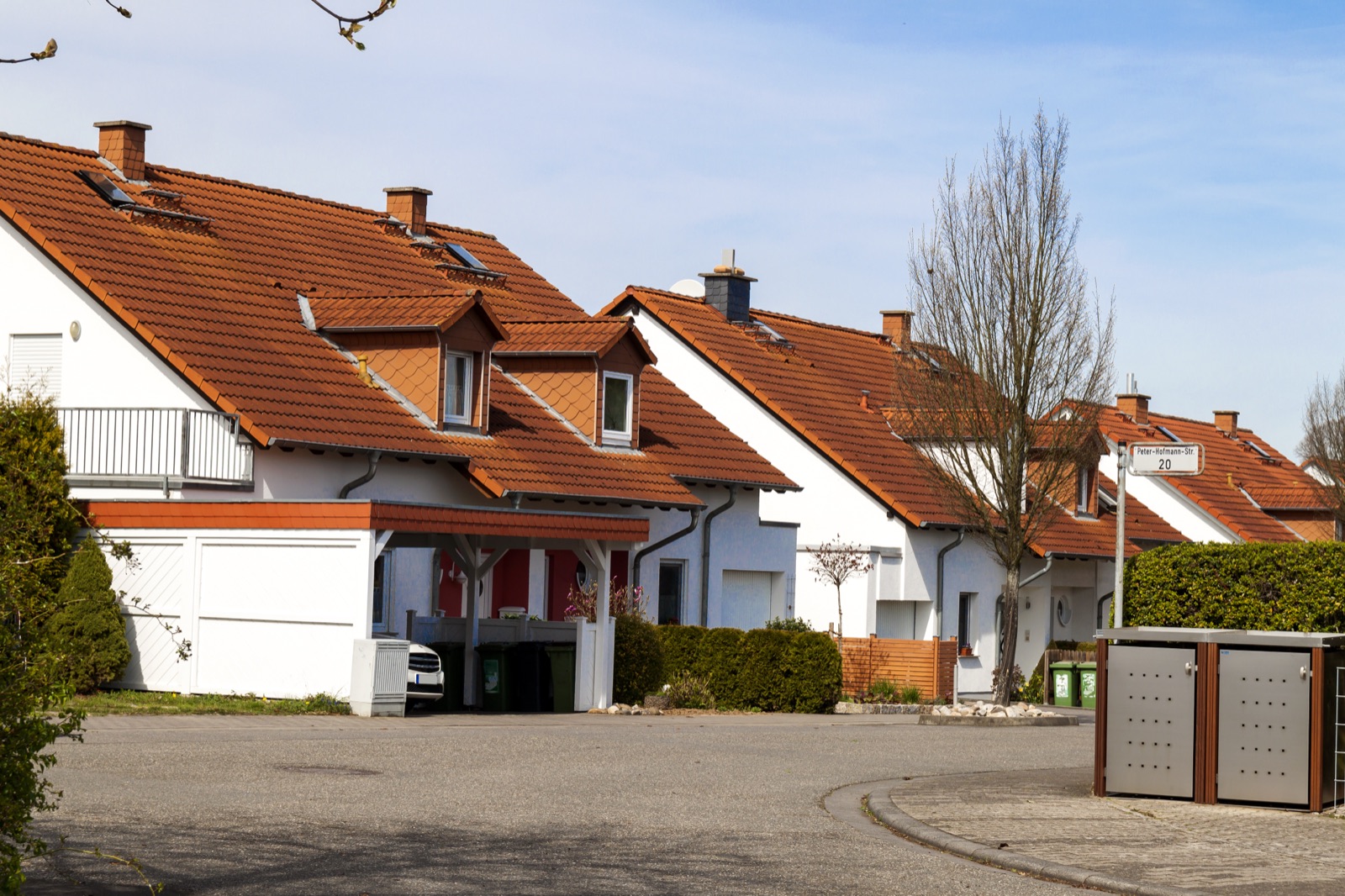 Wohnstraße mit weißen Einfamilienhäusern und roten Ziegeldächern