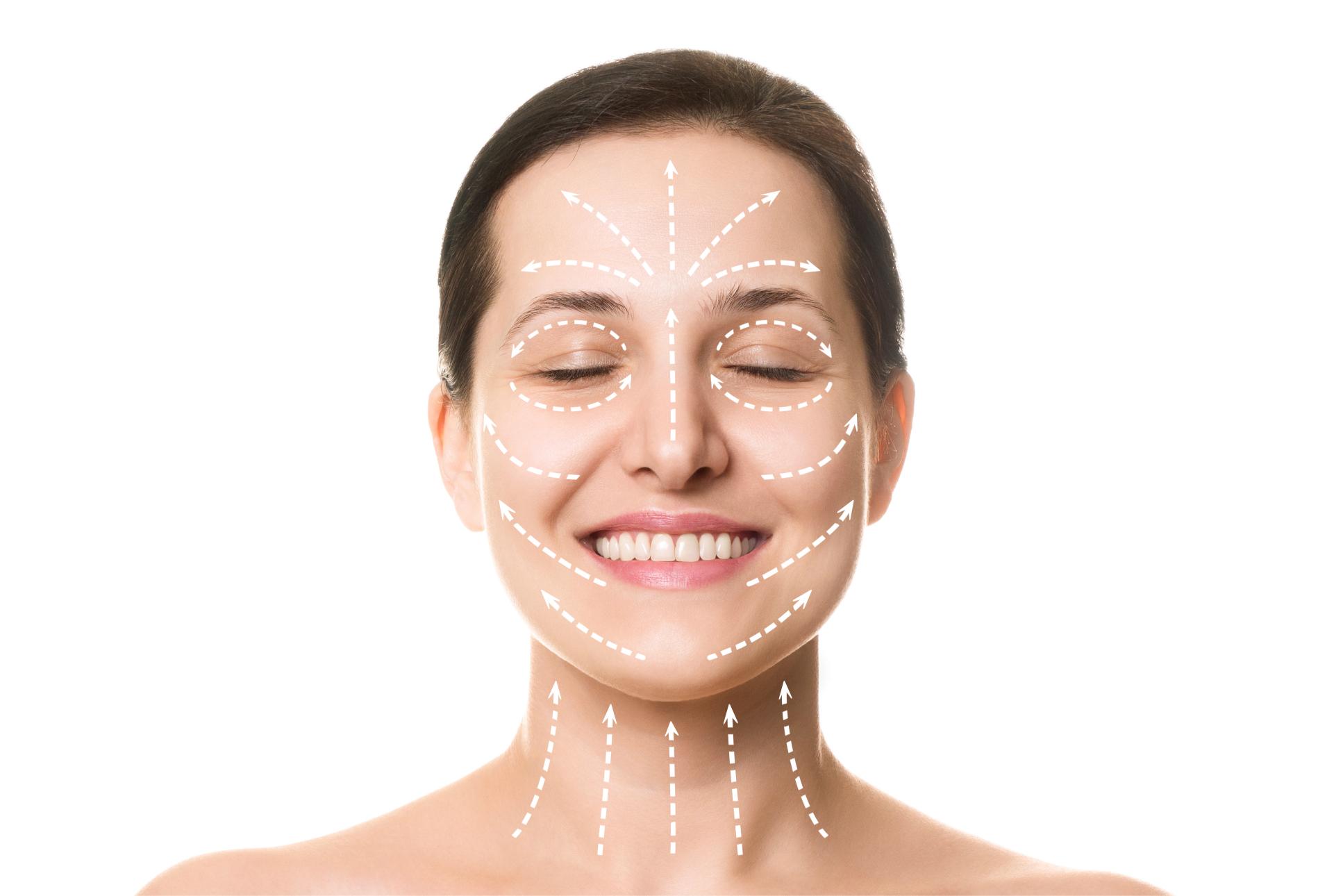Woman with clear skin gently touching her face and smiling against a light blue background.