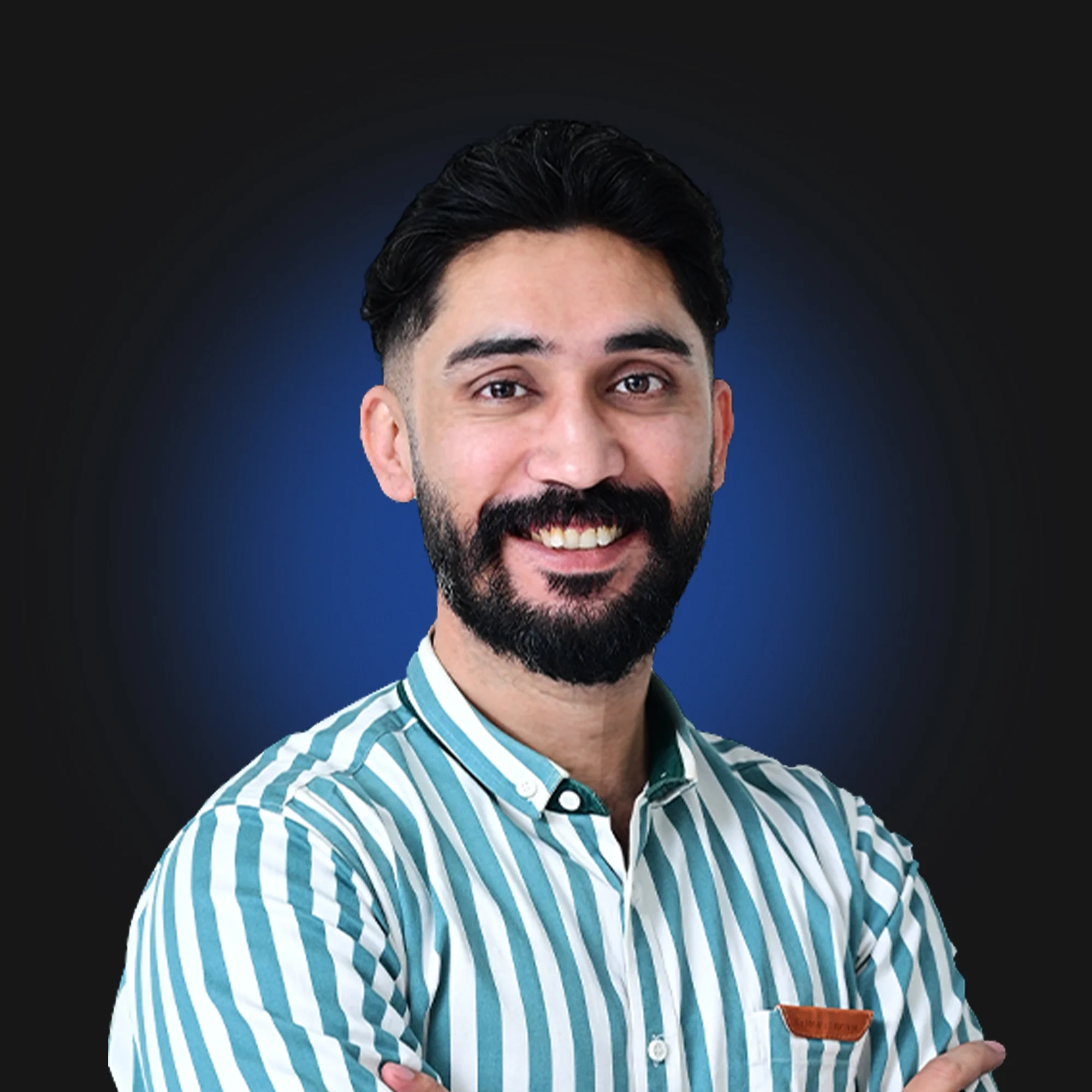 Smiling man with beard and mustache wearing striped shirt with arms crossed on blue-black background.