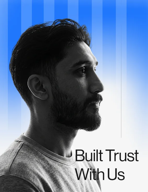 Portrait of a smiling man with short gray hair and beard, wearing a white collared shirt, standing with crossed arms against a blue gradient background.