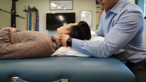 Therapist in a blue shirt holding a patient's head on a pillow during treatment on a massage table.