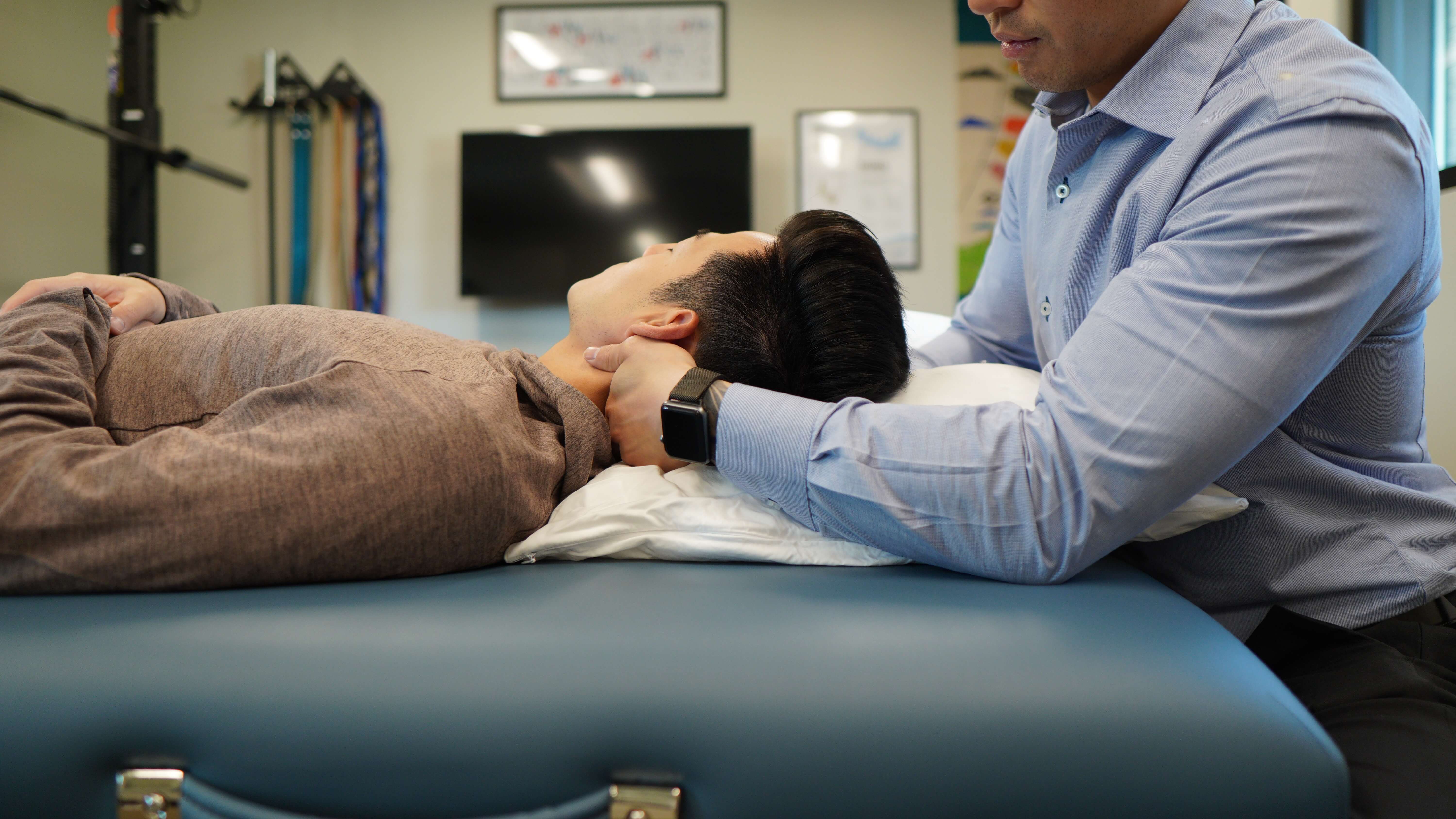 Therapist in a blue shirt holding a patient's head on a pillow during treatment on a massage table.