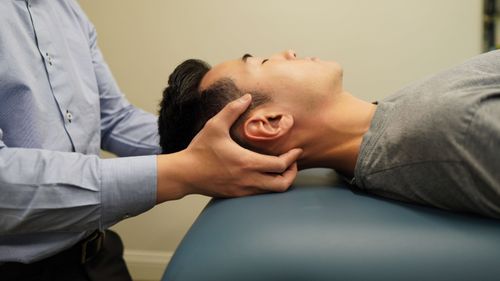 Therapist gently supporting the head of a man lying on a treatment table during a physical therapy session.