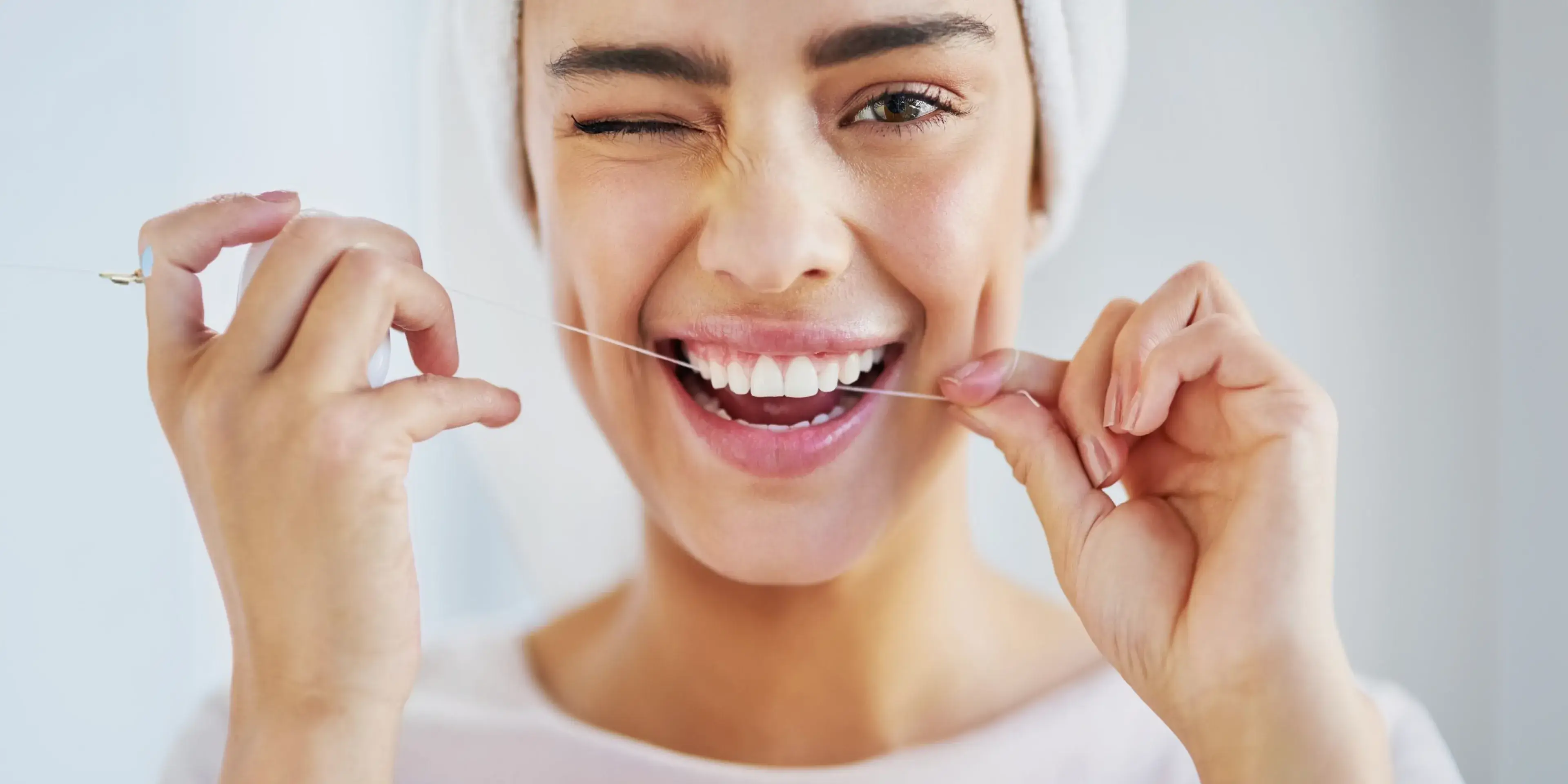 Smiling young woman in a white headband using dental floss to clean her teeth.