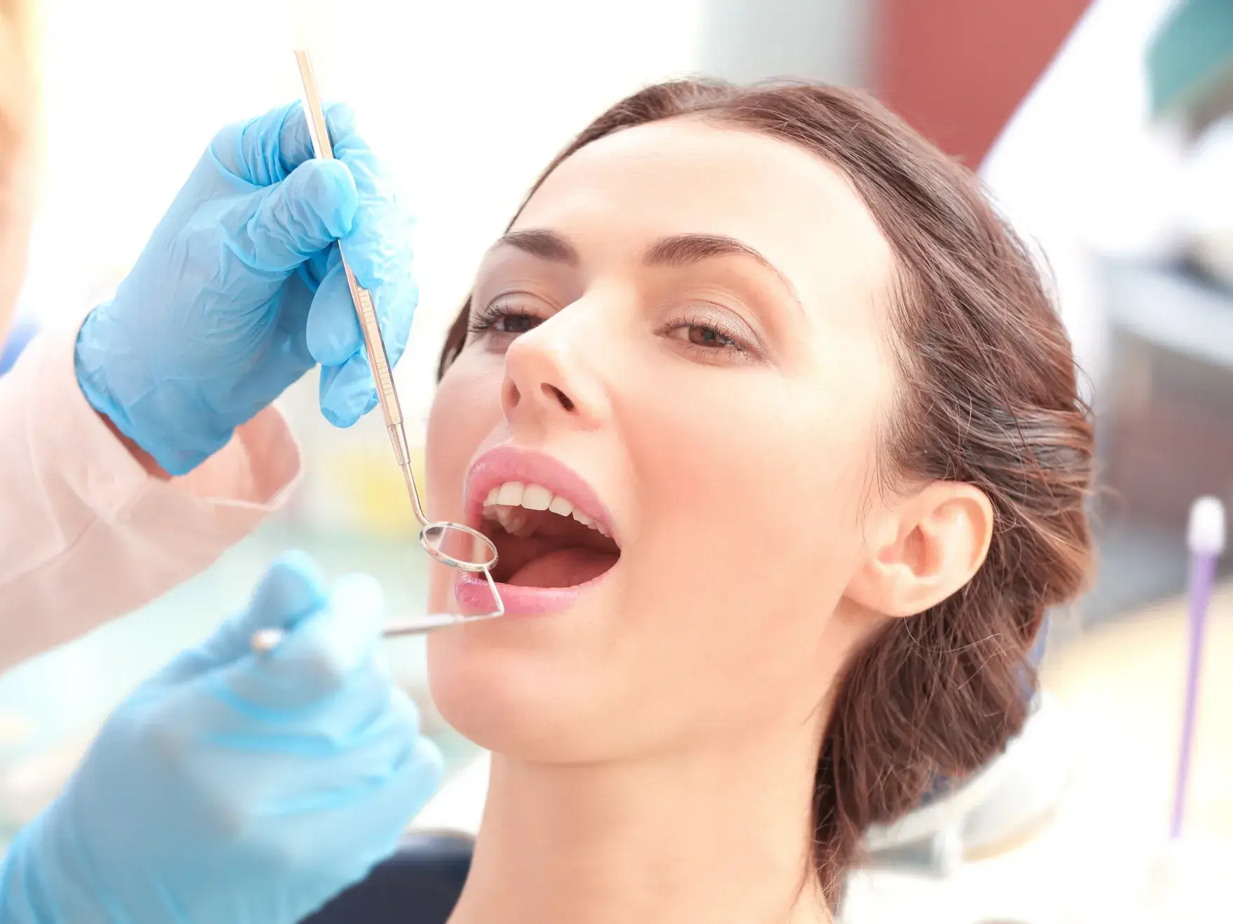 A woman undergoing dental examination with a dentist wearing blue gloves holding dental mirror and probe.