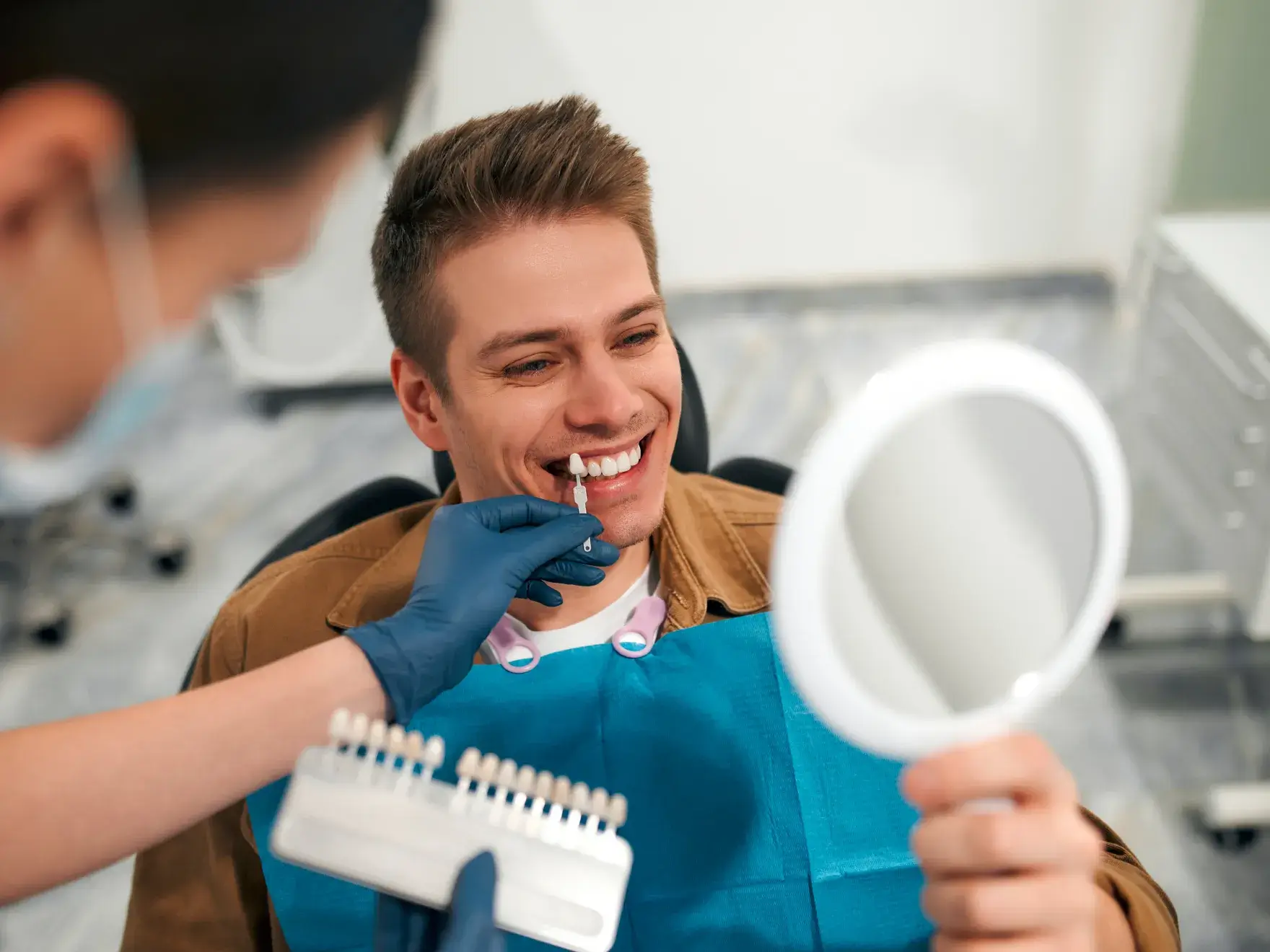 Dentist matching a shade guide to a smiling man's teeth in a dental clinic.