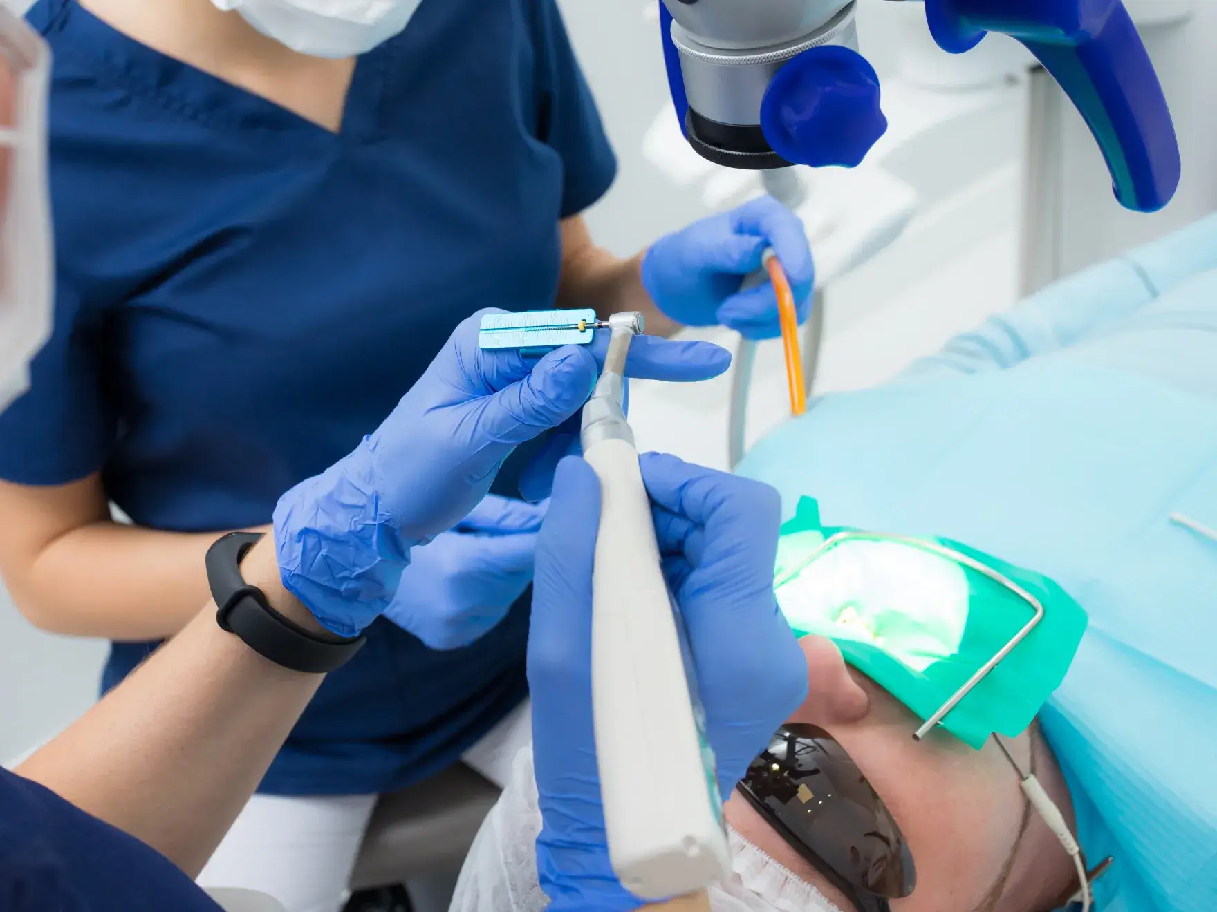 Dentist and assistant using dental tools on patient wearing sunglasses and mouth dam.