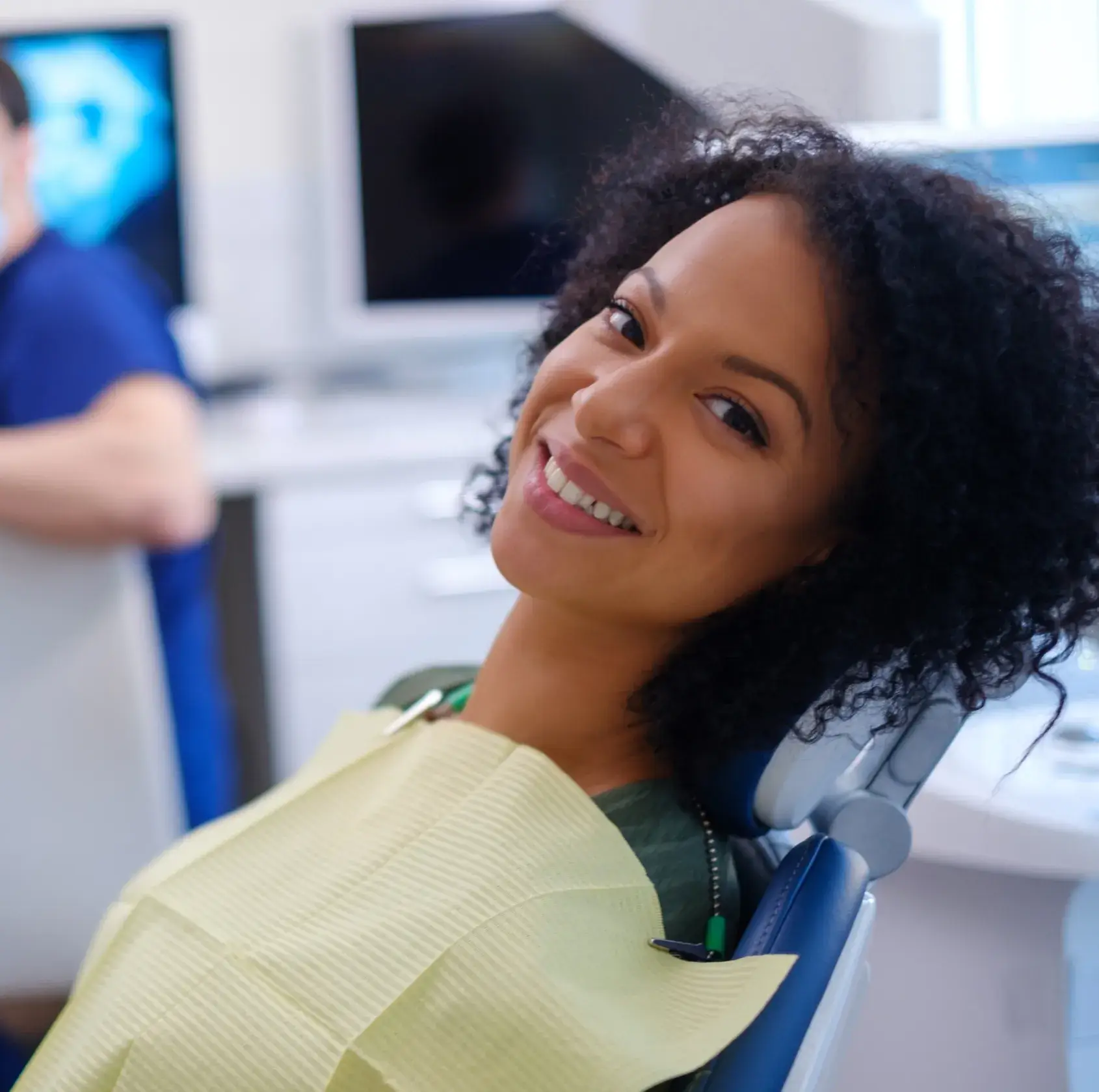 Smiling woman reclined in dental chair wearing a yellow dental bib at the dentist's office.