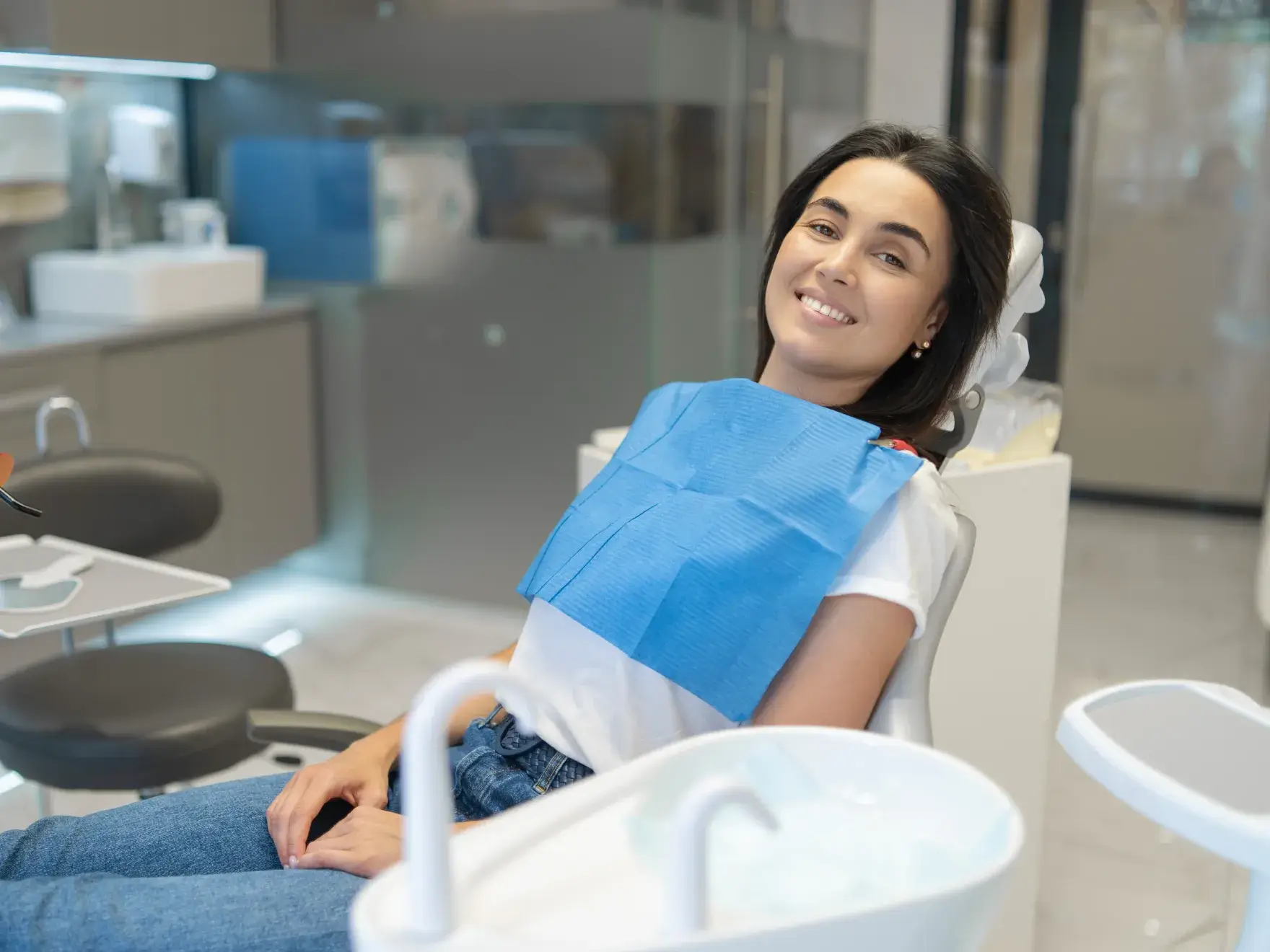 Smiling woman wearing a blue dental bib sitting in a dental chair in a clinic.