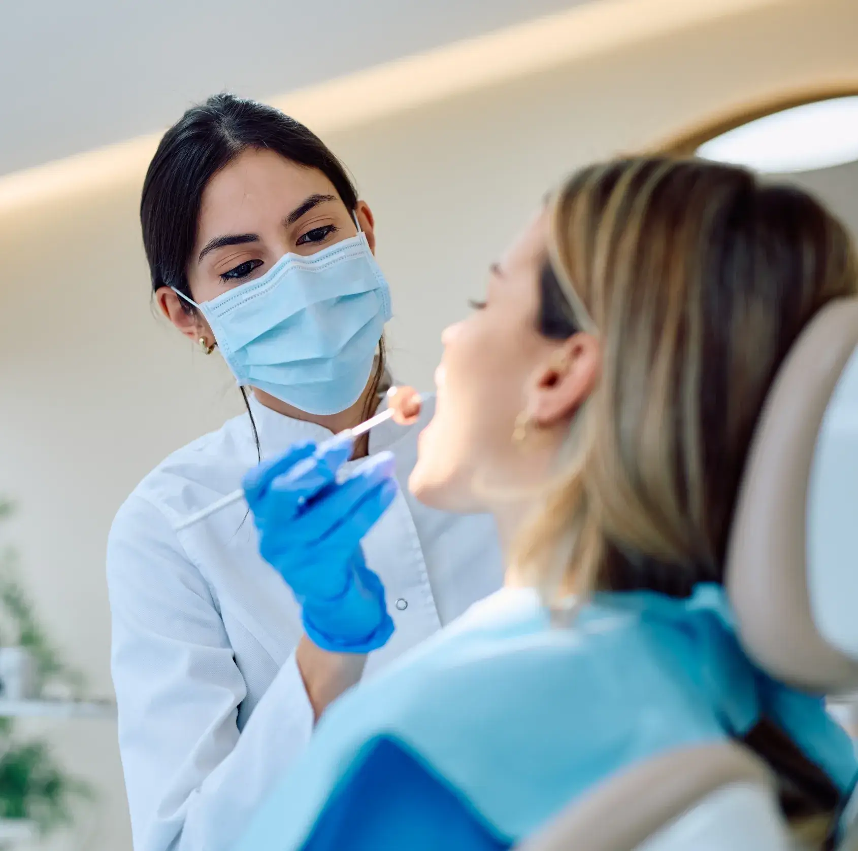 Dentist wearing mask and gloves applying dental veneer to patient's tooth in clinic.