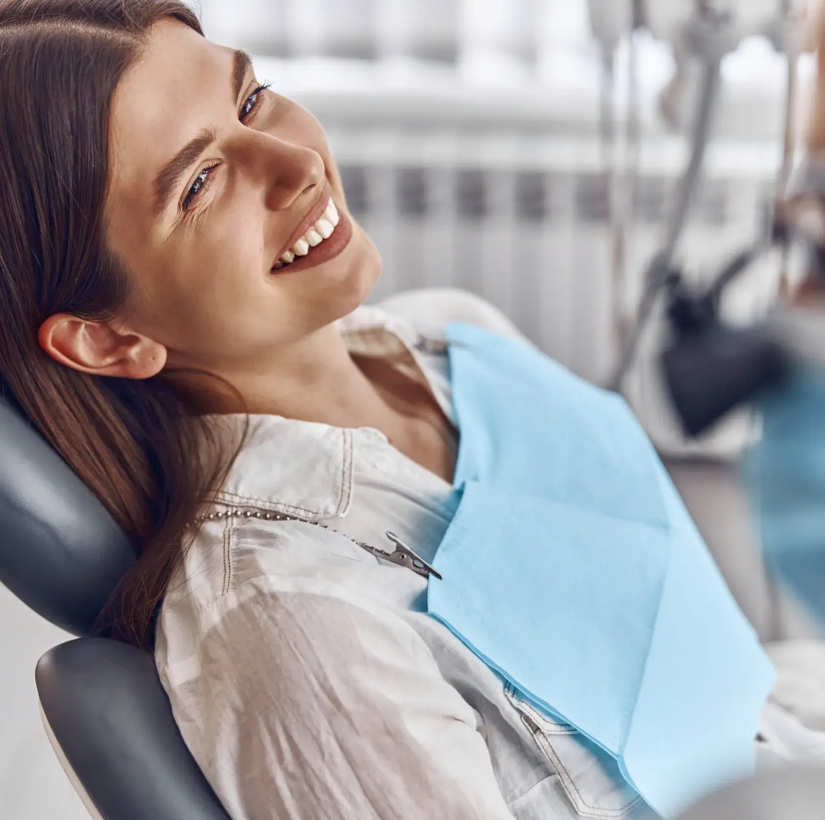 Woman reclining in dental chair with a blue bib, smiling during a dental checkup.