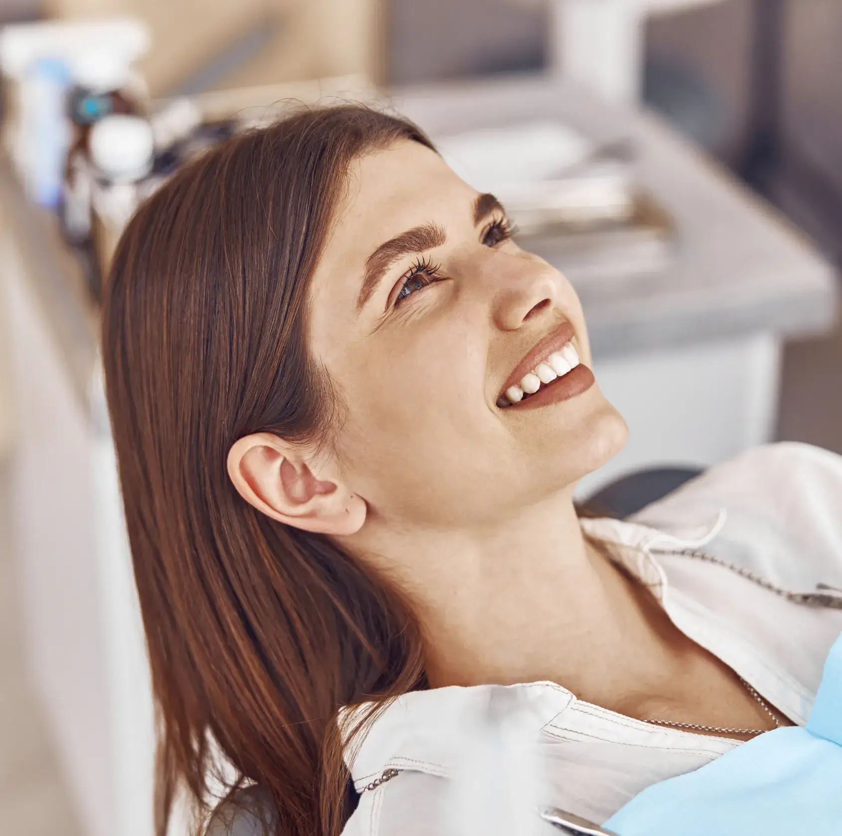Smiling woman with brown hair lying back in a dental chair at a clinic.