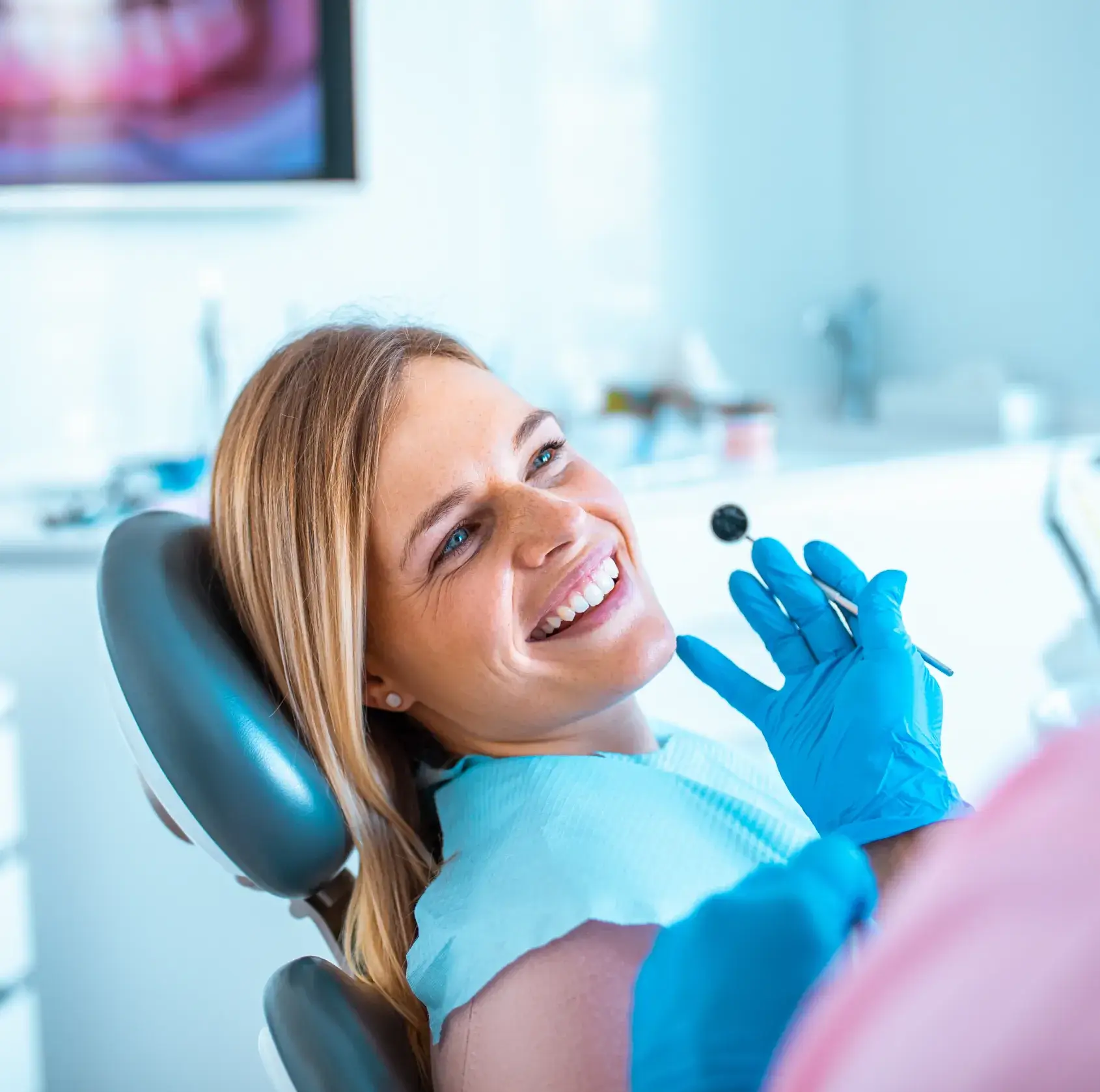 Smiling woman in dental chair during checkup with dentist holding dental mirror.