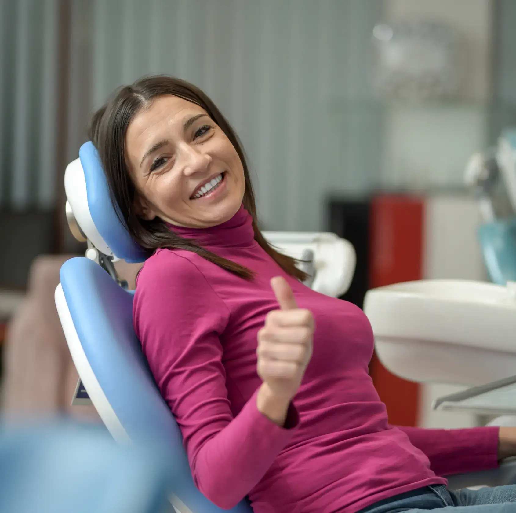 Smiling woman in a purple shirt giving thumbs up while sitting in a dental chair.