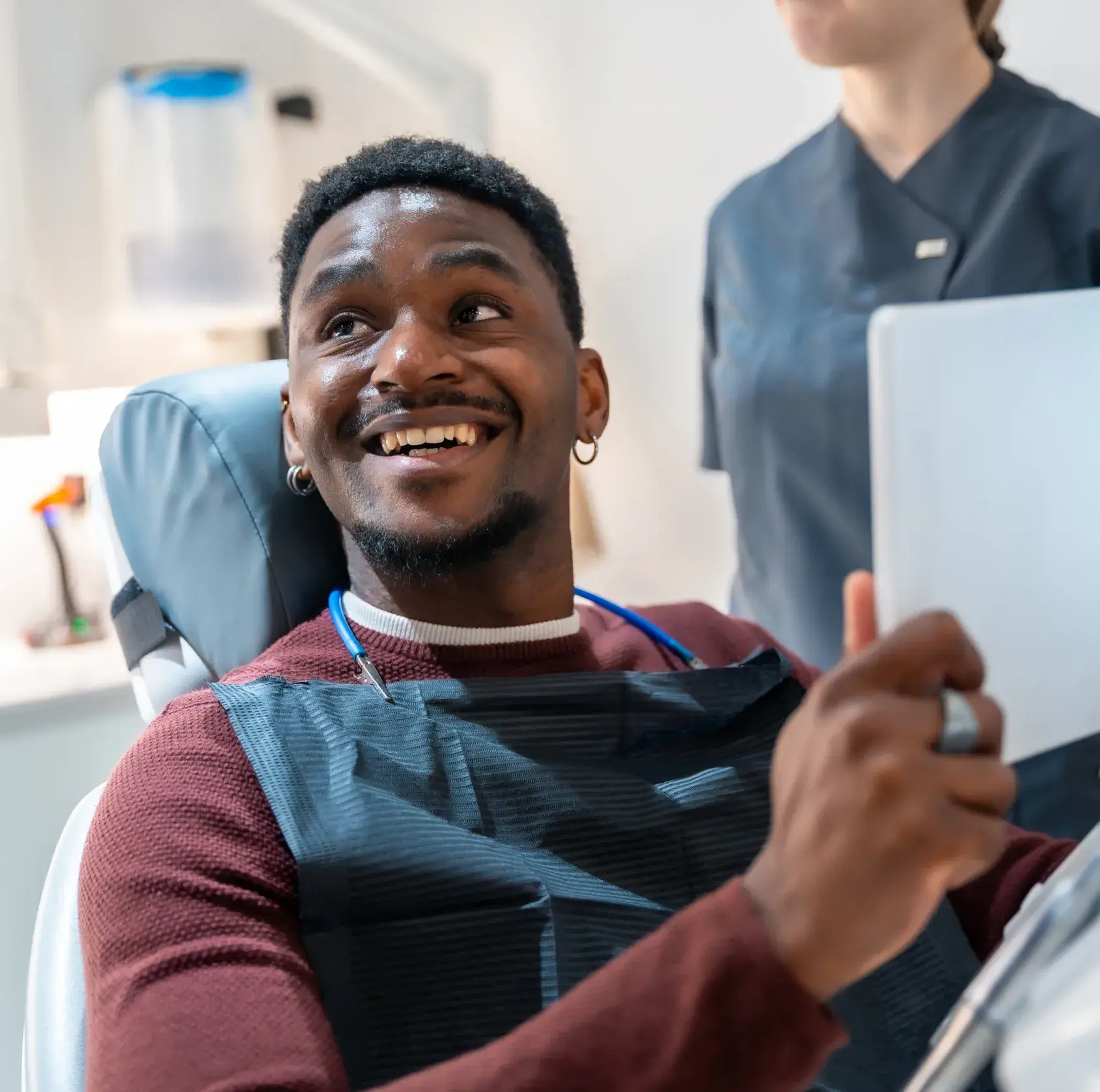 Smiling man in dental chair holding a mirror while a dental professional stands nearby.