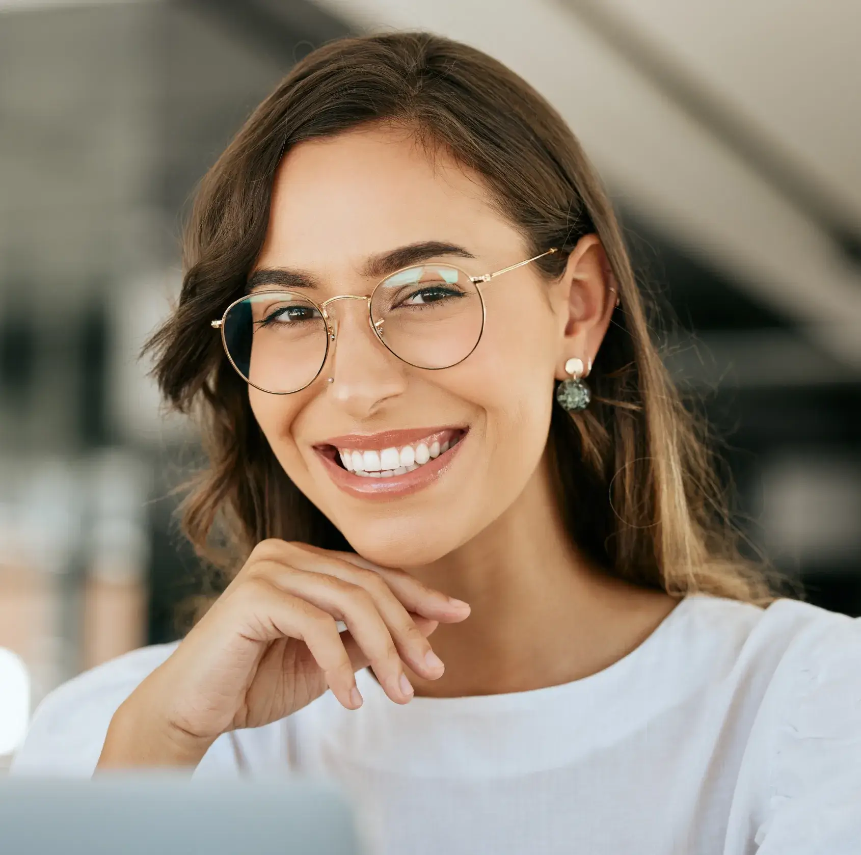 Smiling woman with glasses showing bright white teeth and resting her chin on her hand.