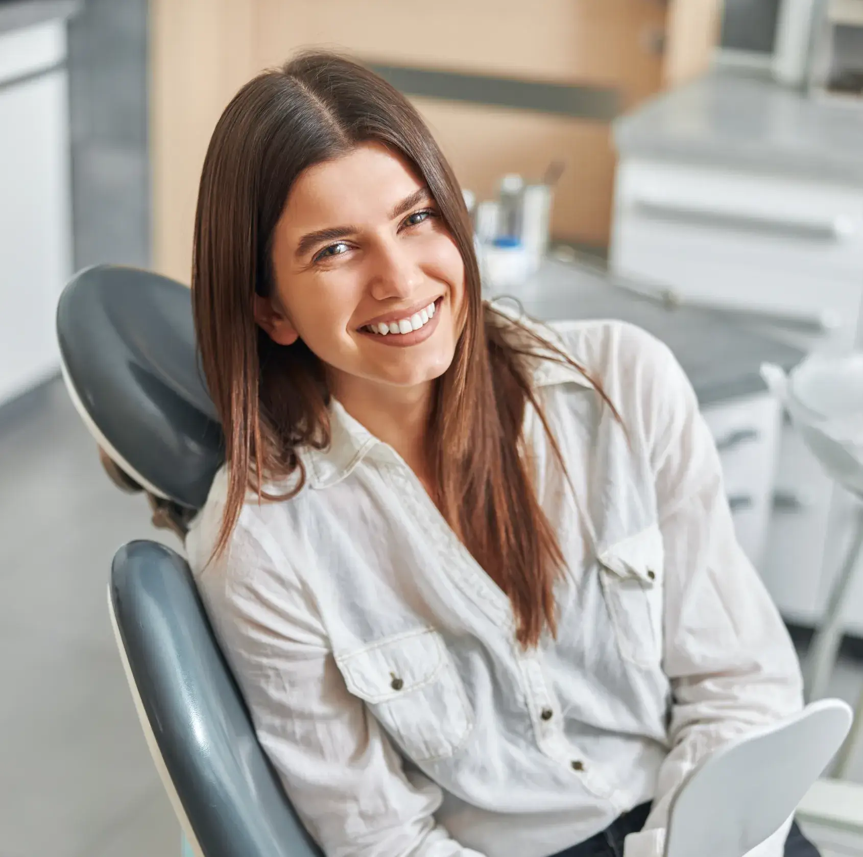 Smiling woman with long brown hair sitting in a dental chair in a clinic.
