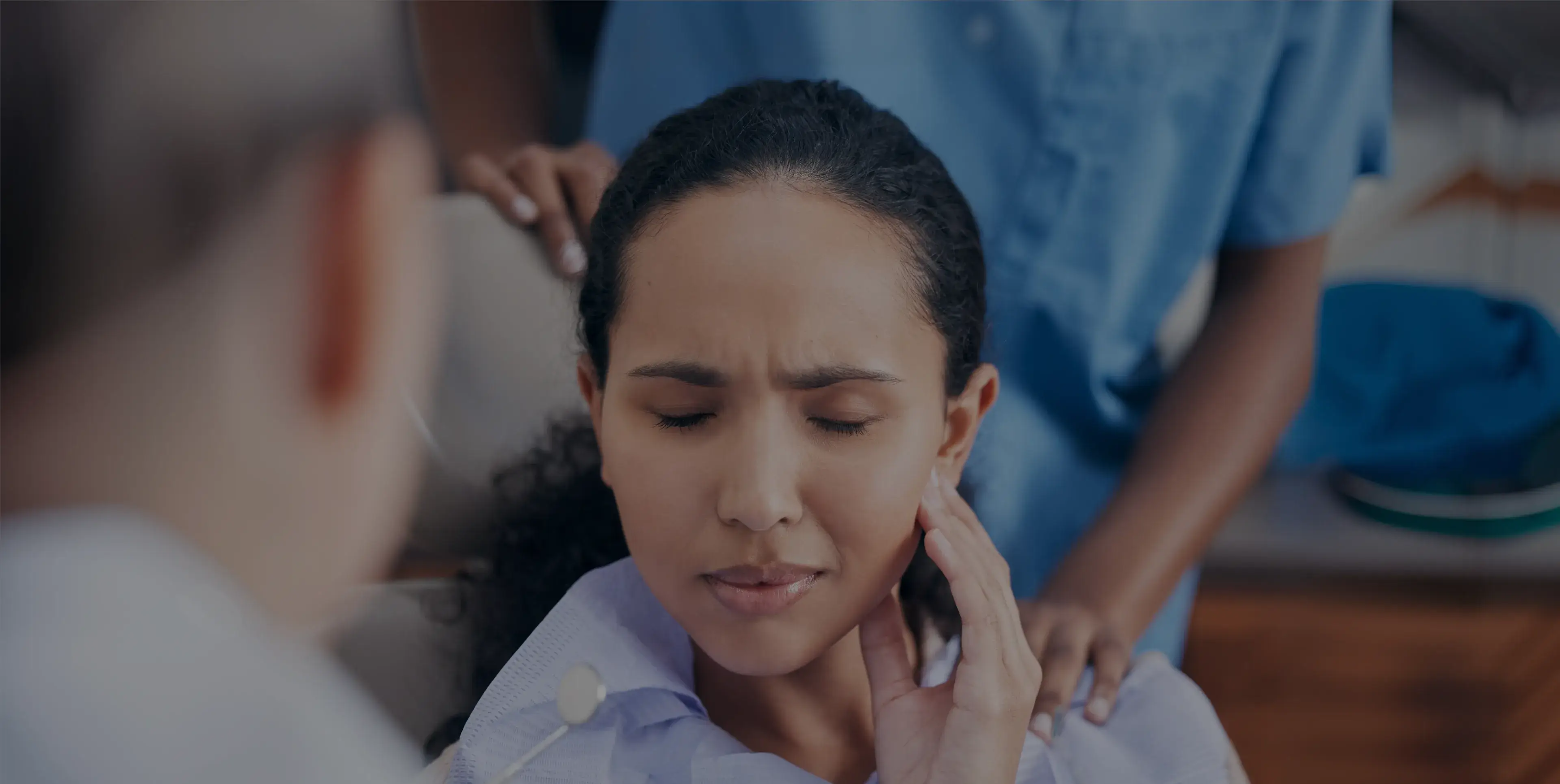Woman with eyes closed touching her jaw in pain while a healthcare worker comforts her.